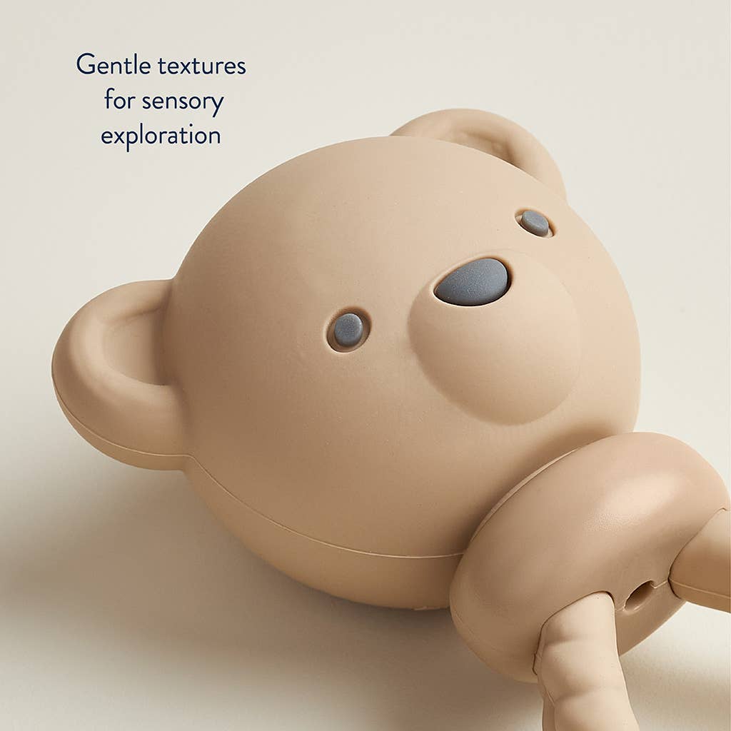 Beige teddy bear toy with text 'Gentle textures for sensory exploration' on a light background