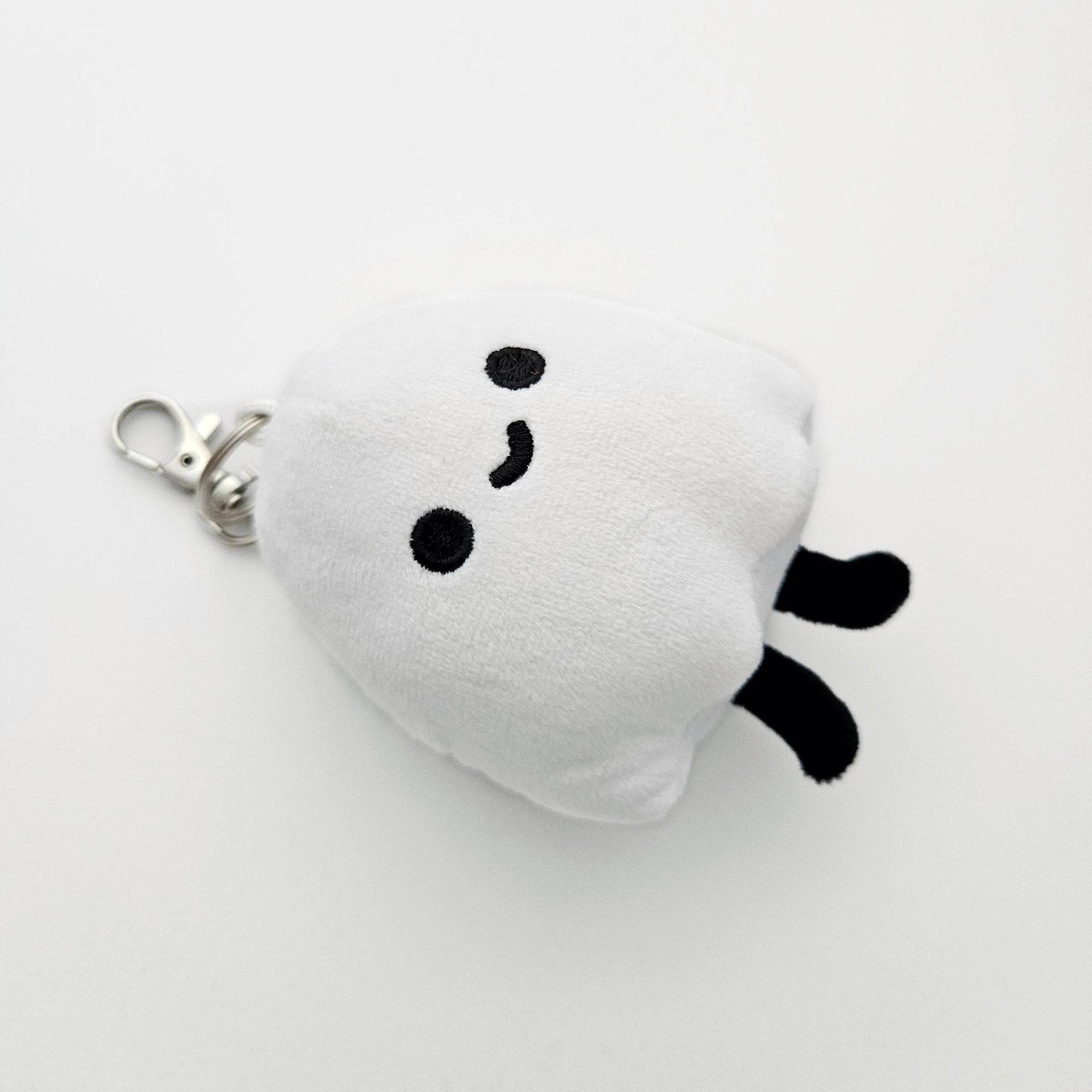White plush keychain with black accents on a light gray background