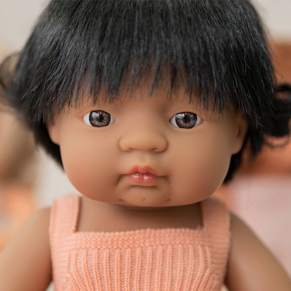 Close-up of a doll with black hair and a pink outfit against a blurred background