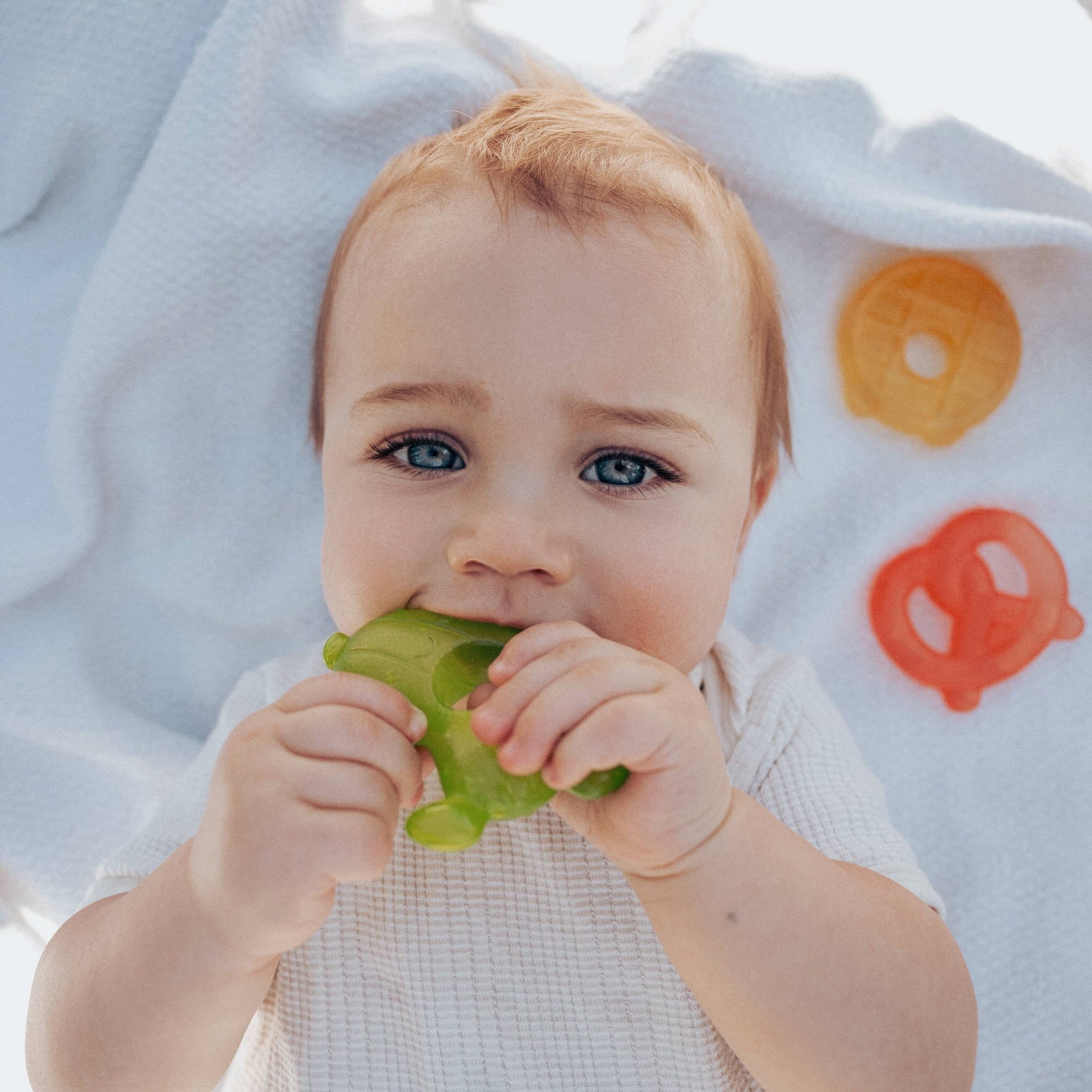 Baby chewing on a green object with colorful letters in the background