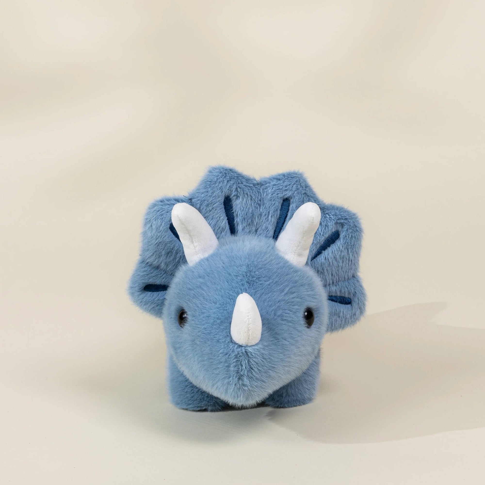 Blue plush triceratops toy on a beige background