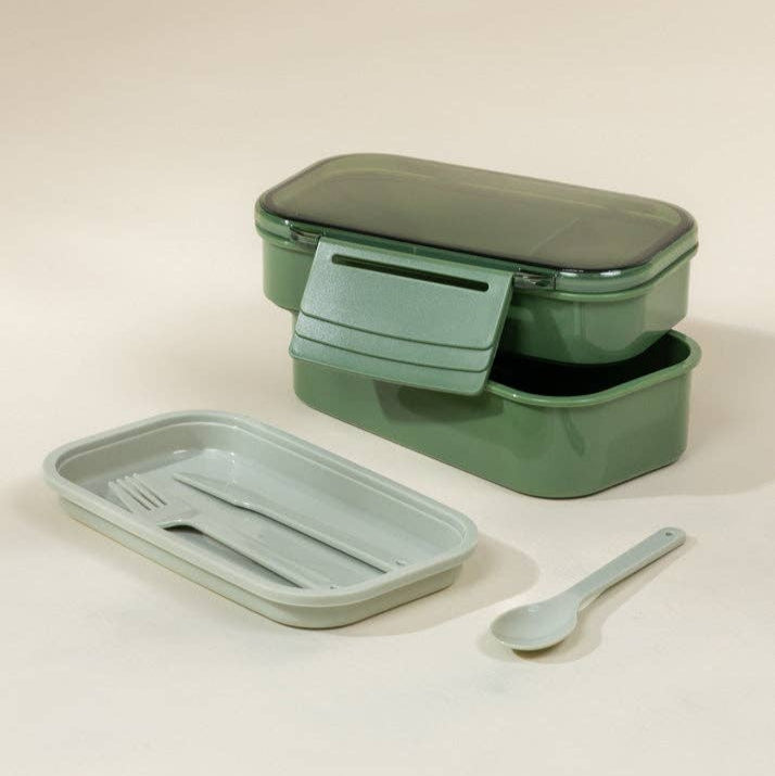 Green lunch box with compartments and utensils on a beige background