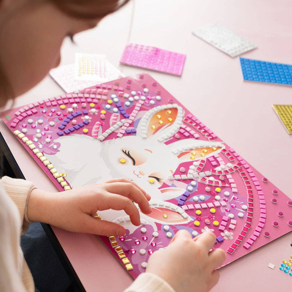 Child working on a craft project with colorful materials on a pink surface