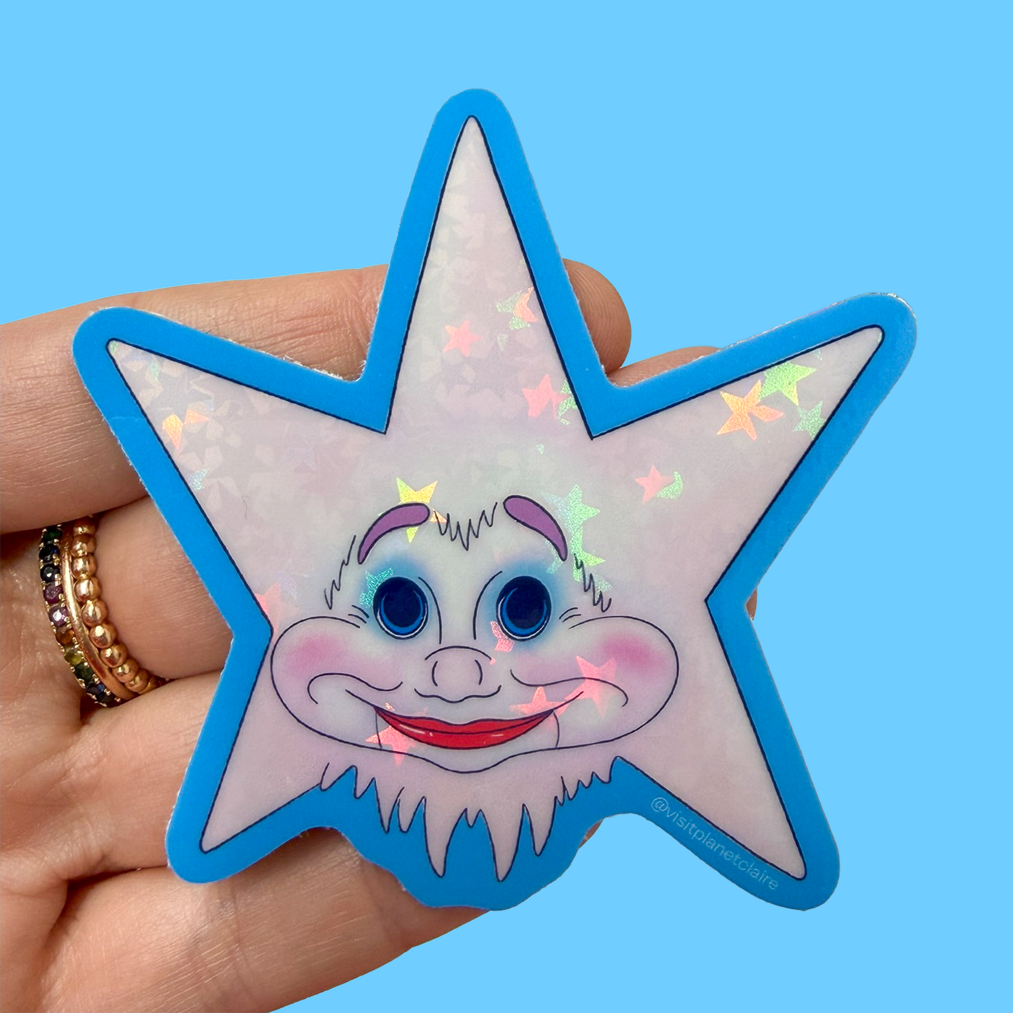 Star-shaped sticker with a cartoon character held by a hand against a blue background