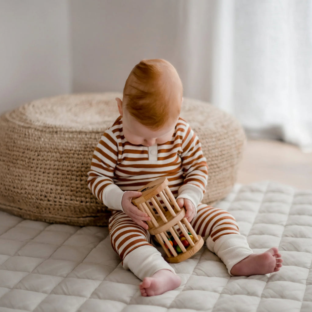 Baby in striped pajamas playing with a wooden toy on a bed.
