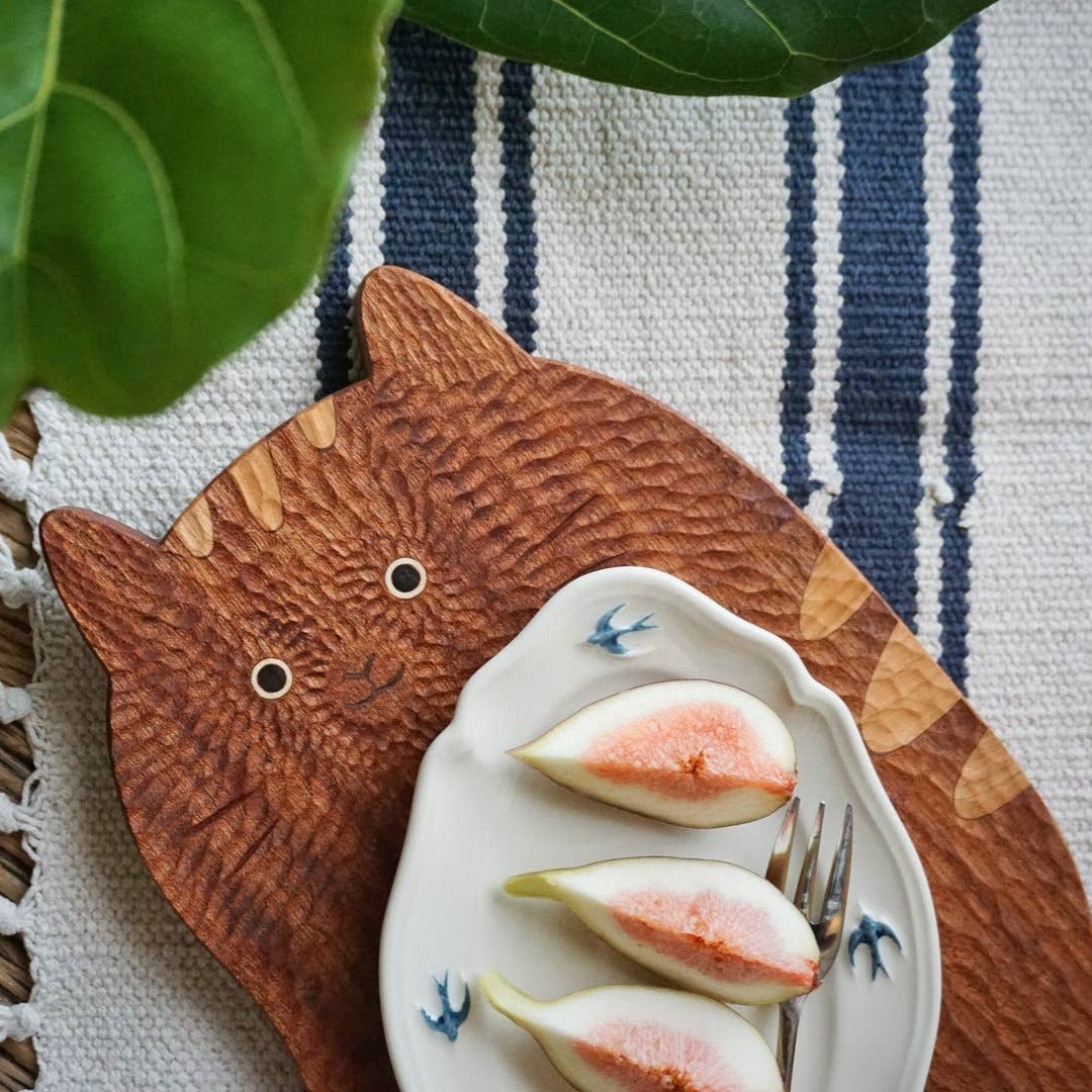 Cat-shaped wooden coaster with a small plate of figs on a striped fabric background