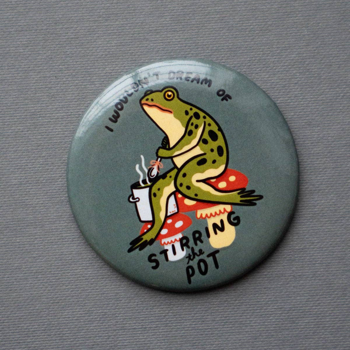 Button badge with a frog design on a gray background