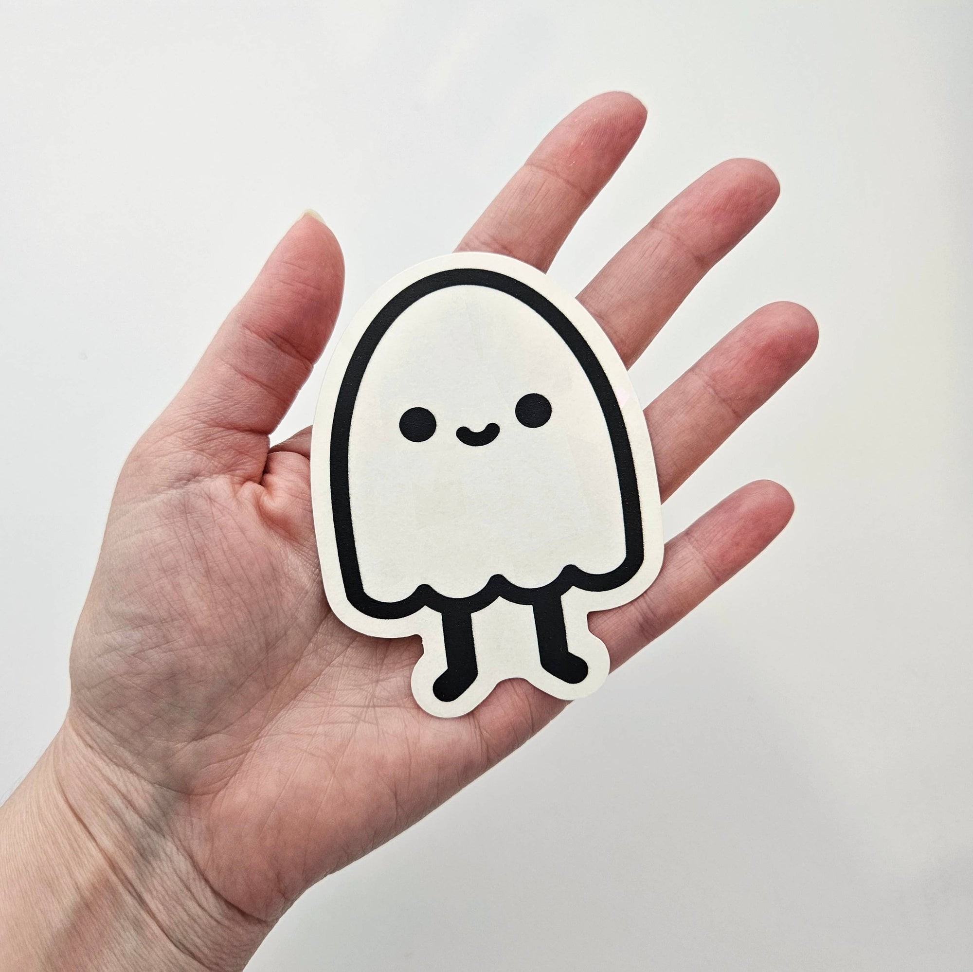 Hand holding a cute ghost-shaped sticker against a plain background