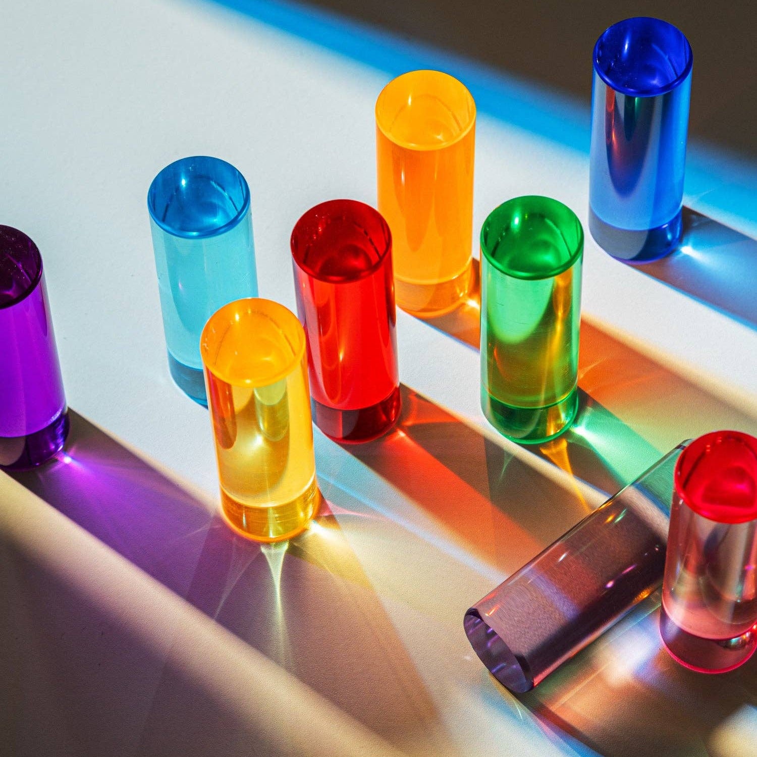 Colorful transparent tubes on a reflective surface with a light source creating shadows.