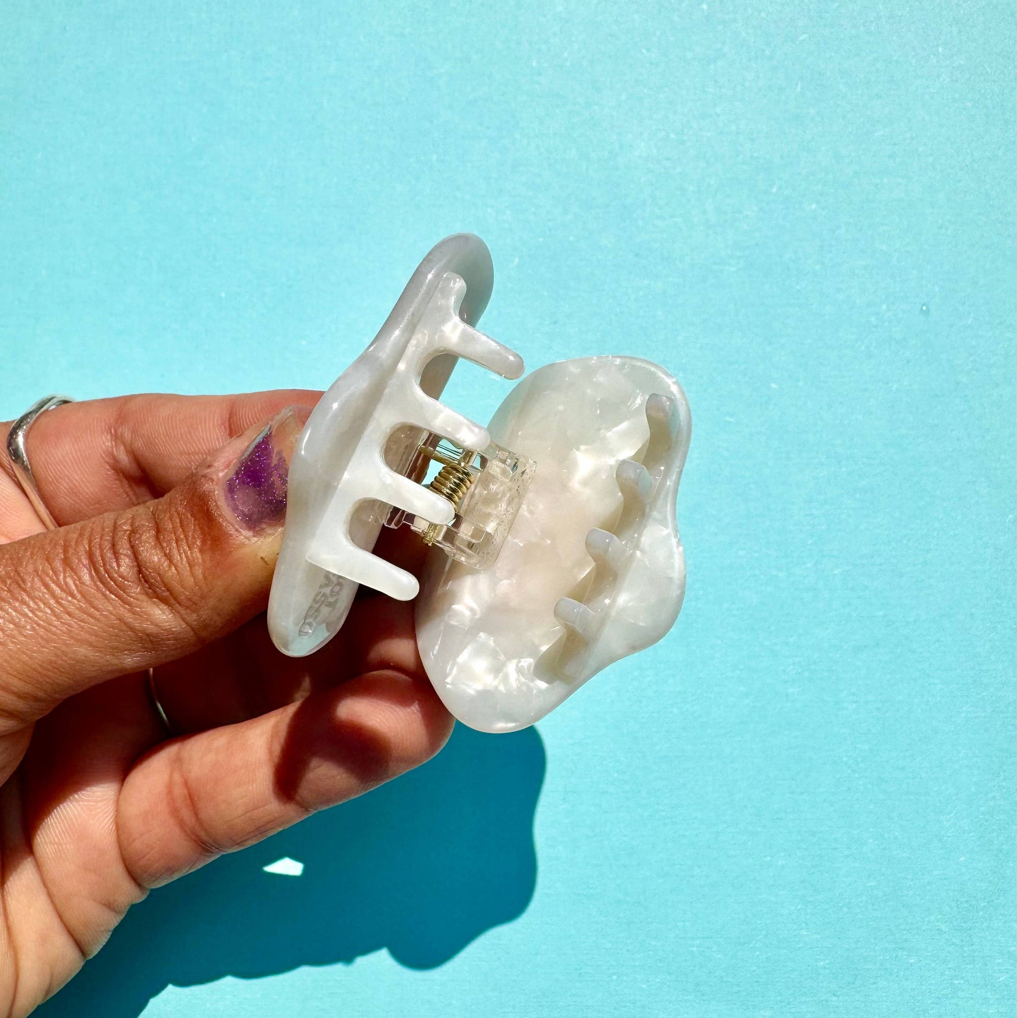 Hand holding a white hair clip against a light blue background