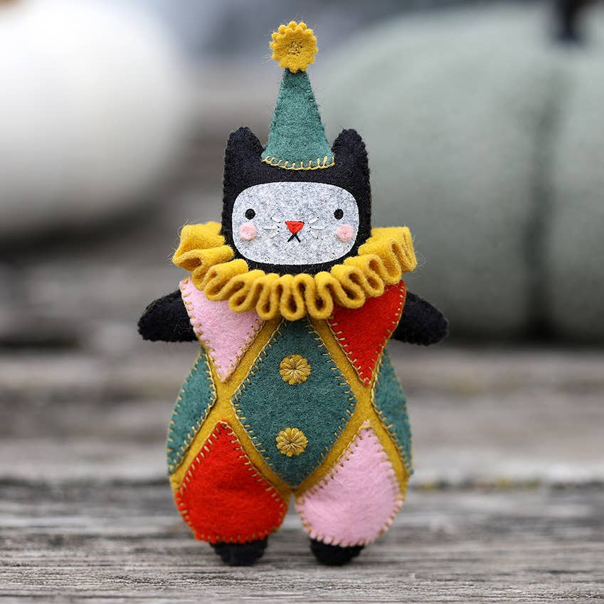 Colorful felt clown cat toy on a wooden surface with pumpkins in the background