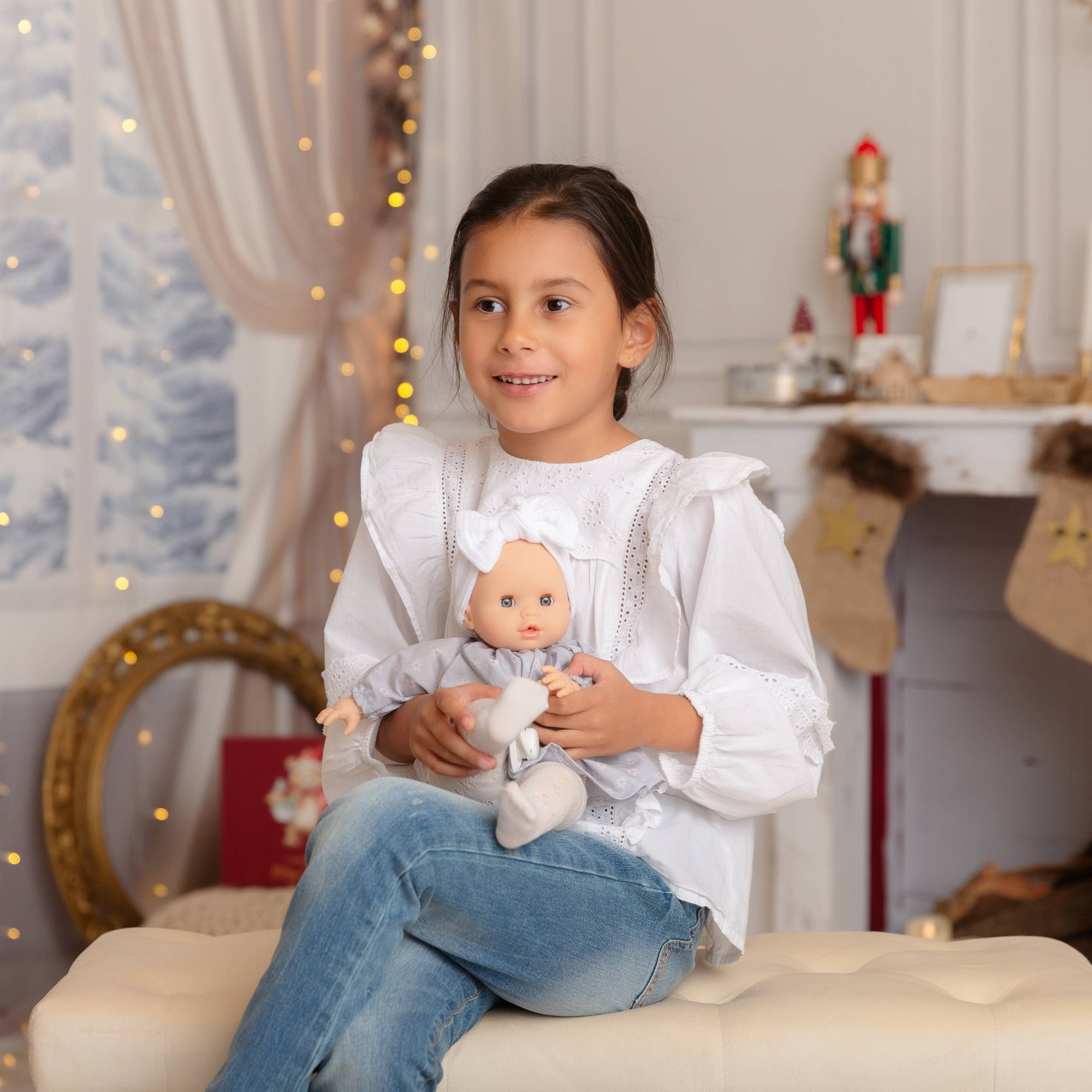 Young girl holding a babydoll in a decorated room with lights and stockings.