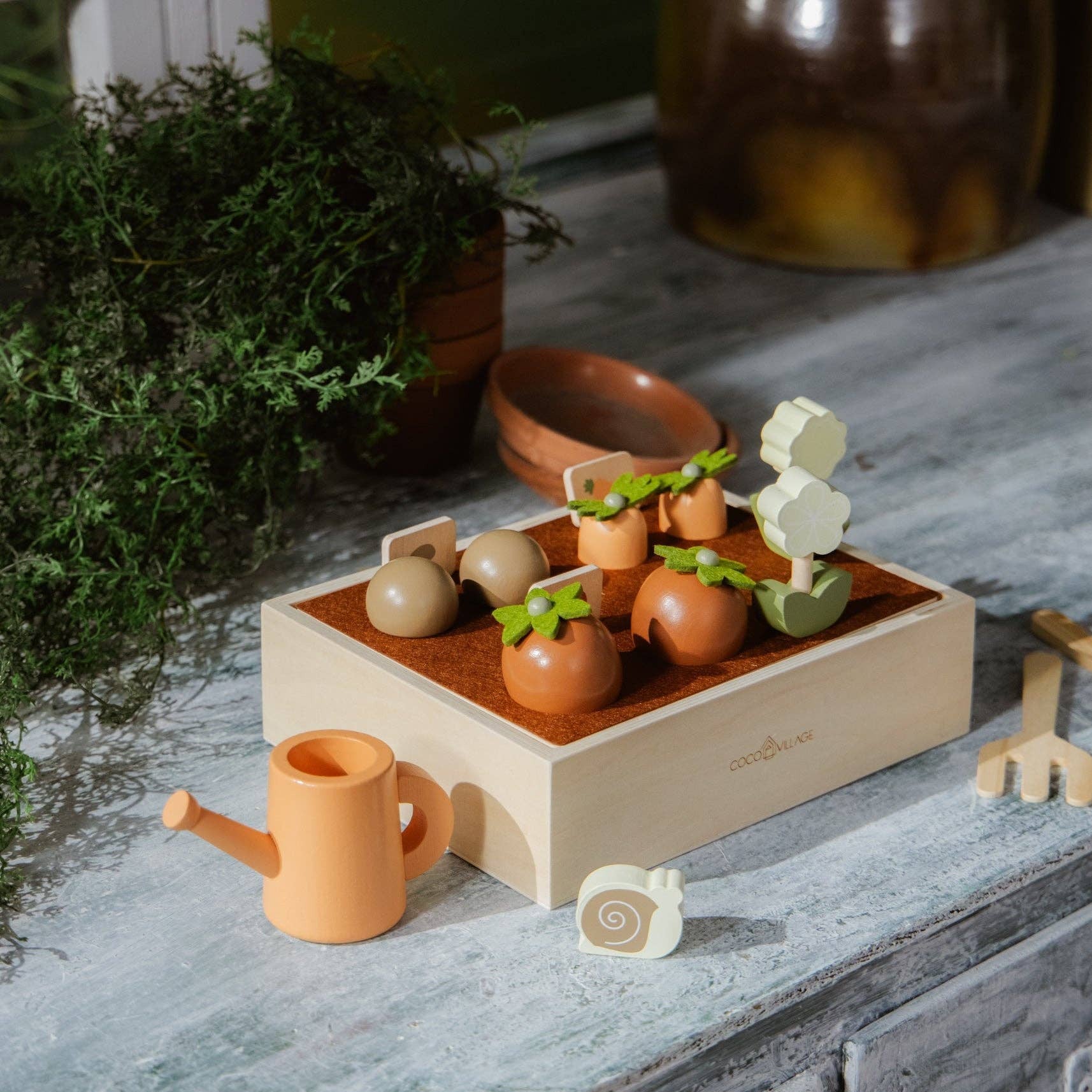 Wooden toy garden set with plants and a watering can on a rustic wooden surface.