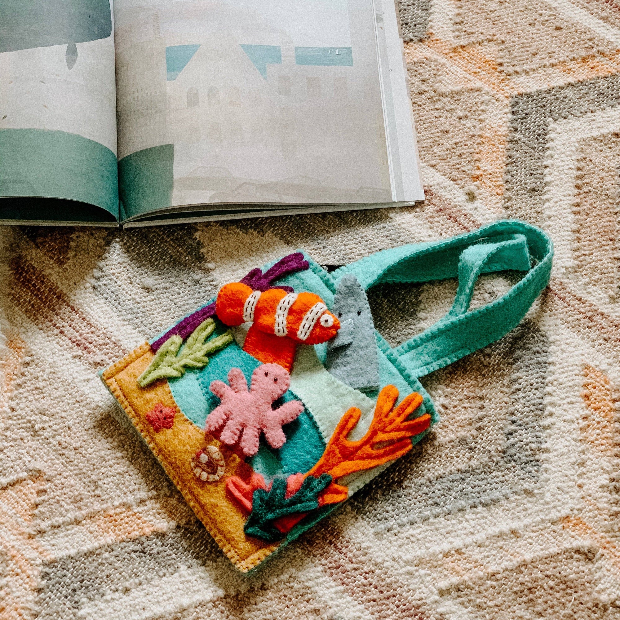 Felt book with colorful marine-themed illustrations on a textured surface next to an open book.