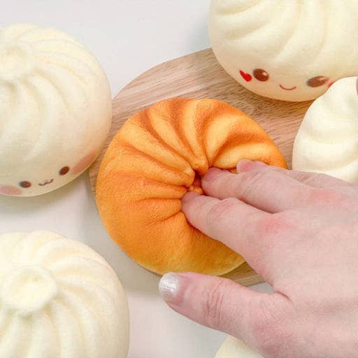 Hand interacting with a soft, round orange toy on a white surface with other similar toys.