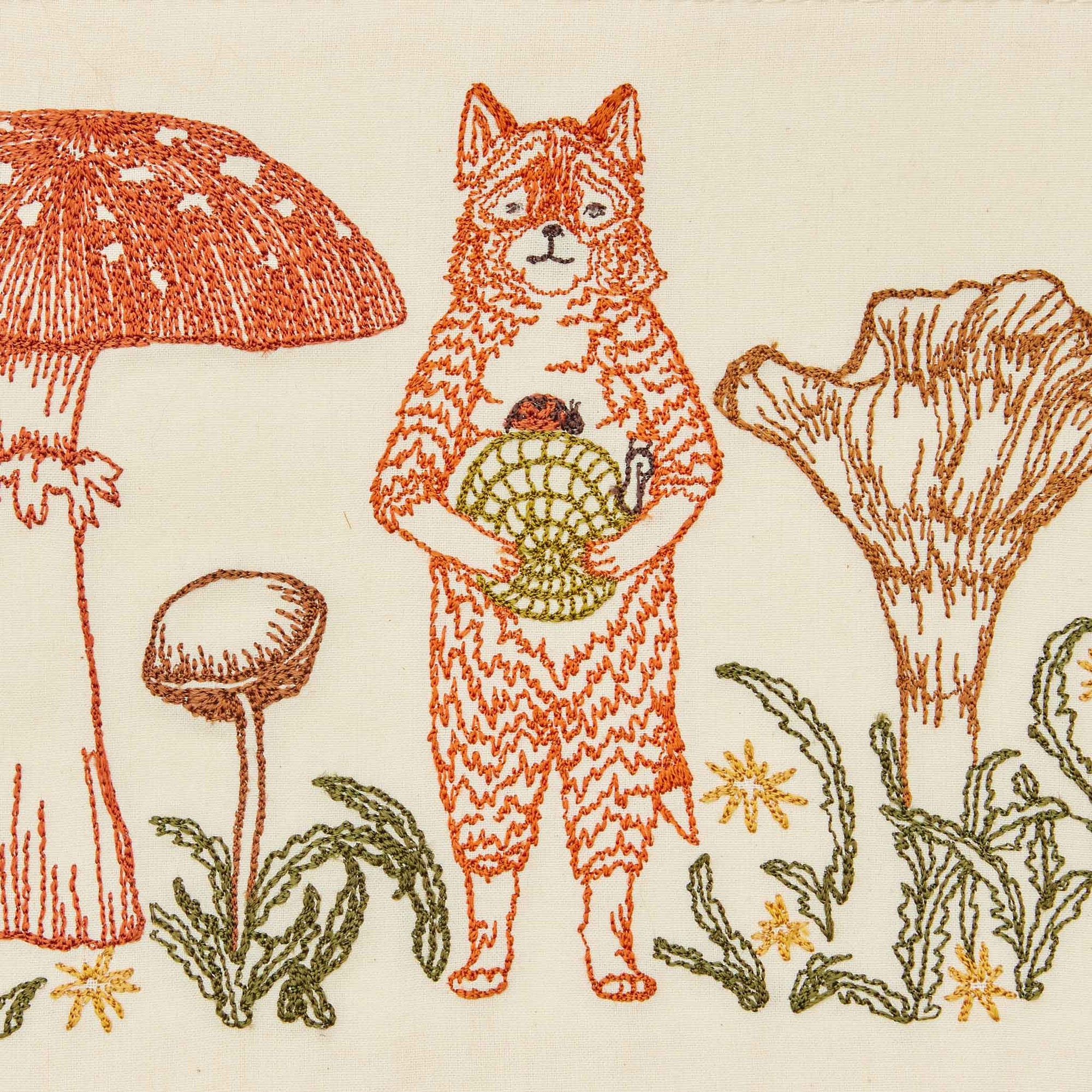 Embroidered design of a fox holding a snail, surrounded by various mushrooms and plants on a beige background.