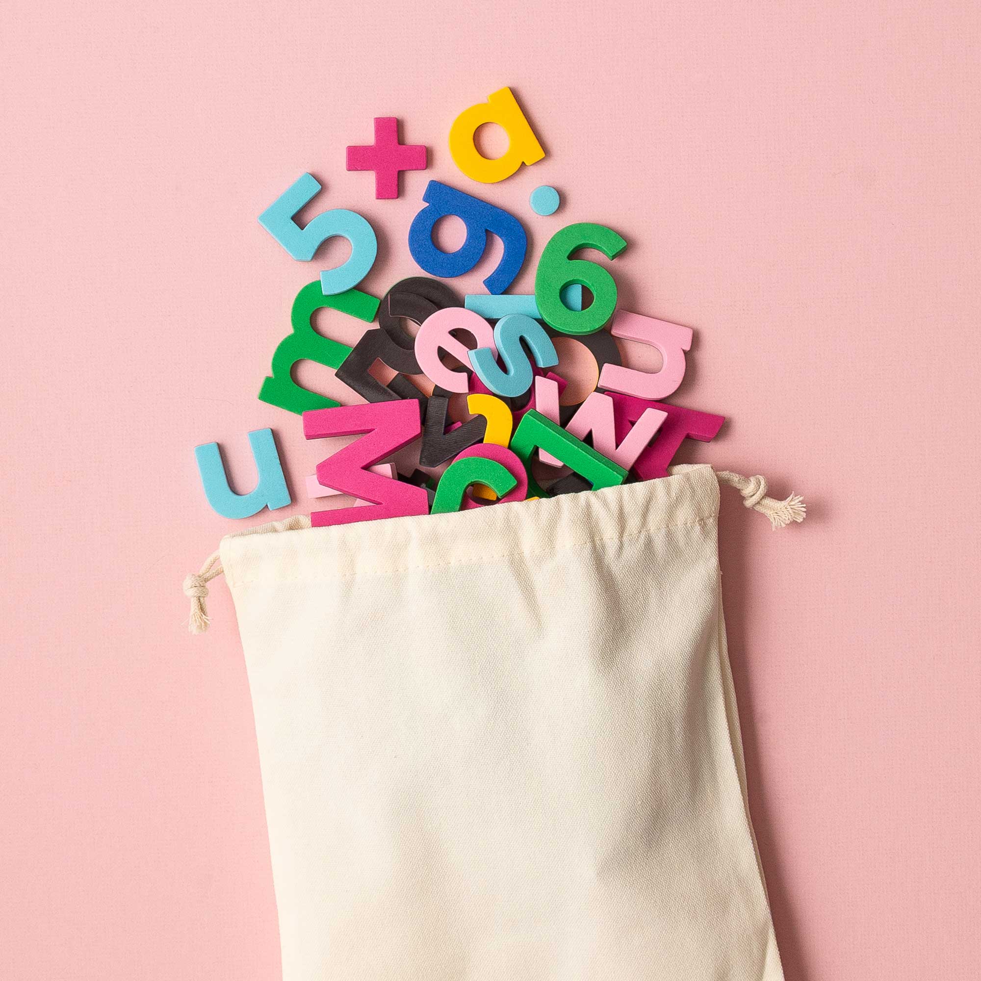 Colorful magnetic letters spilling out of a white drawstring bag on a pink background