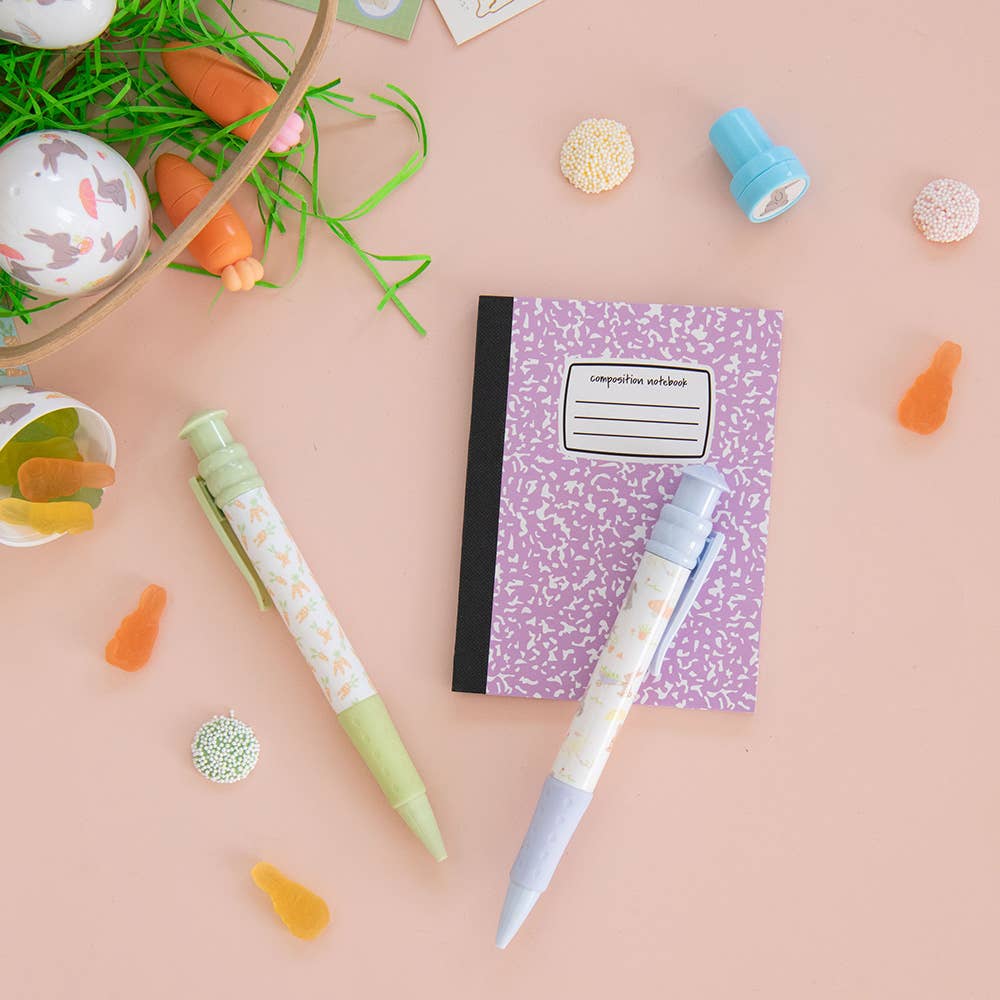 Two pens and a notebook on a pink surface with Easter decorations.