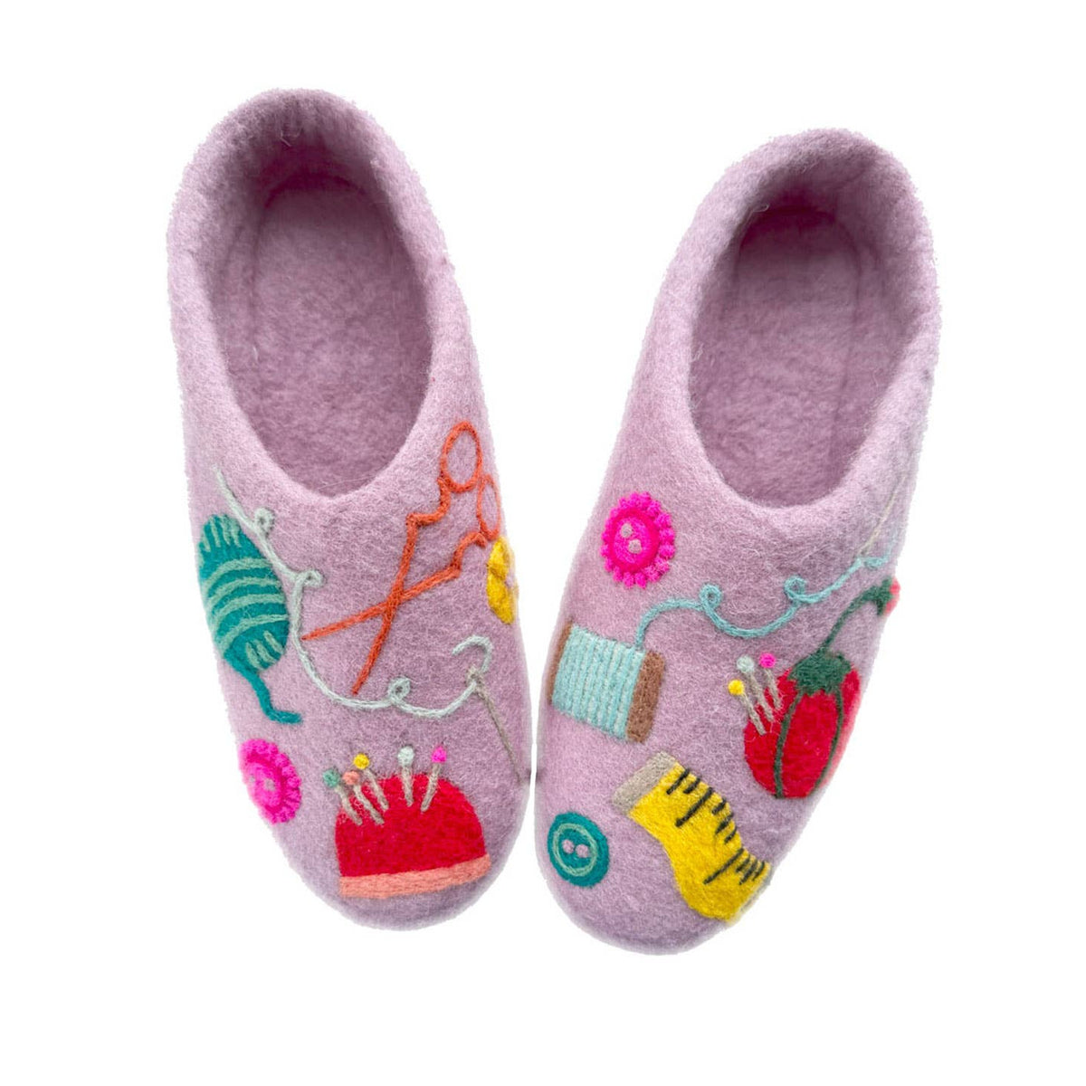 A pair of lavender felt house slippers decorated with colorful embroidered sewing-themed motifs including yarn, scissors, thread, pins, and a strawberry on a plain white background.
