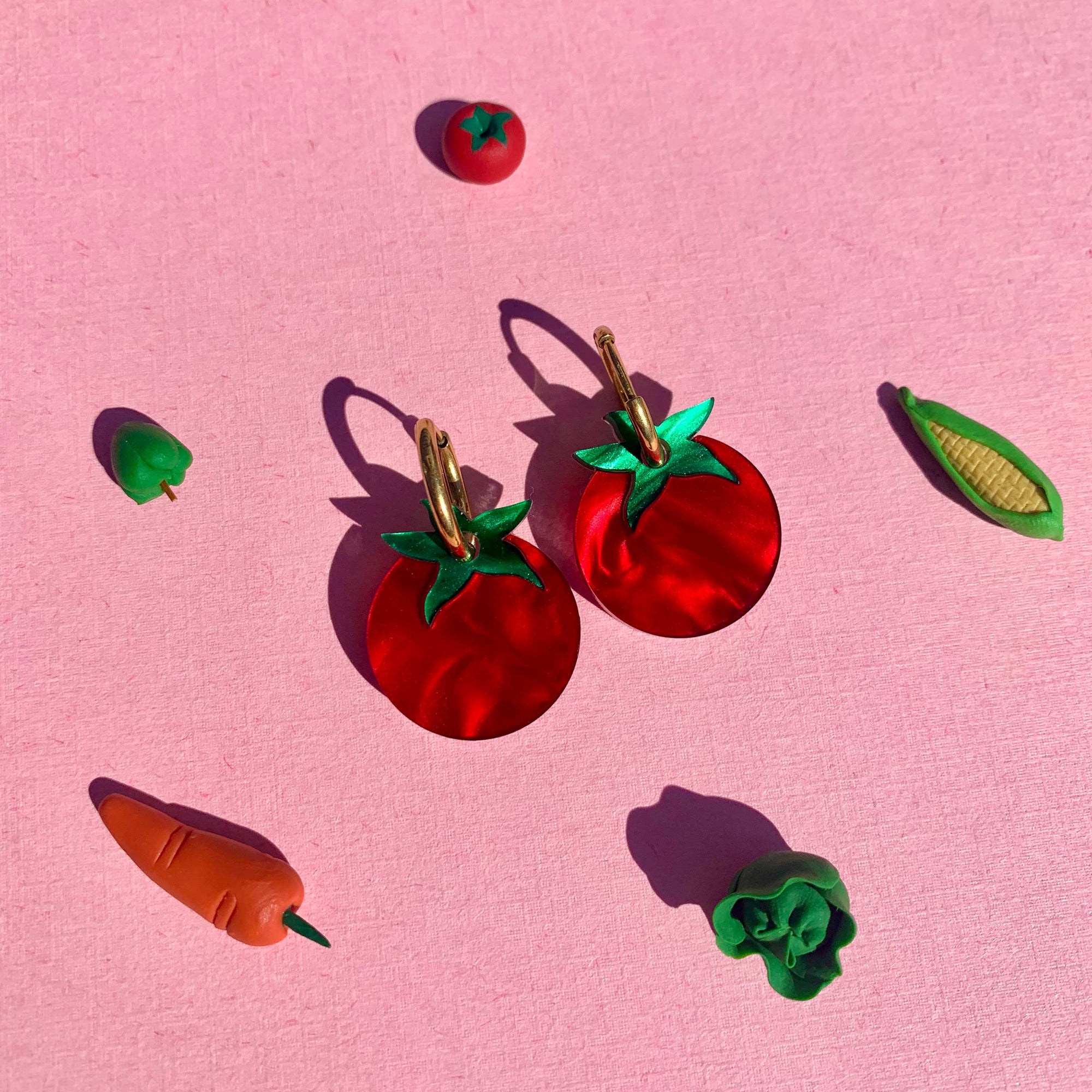 Red tomato-shaped earrings with green leaves on a pink background