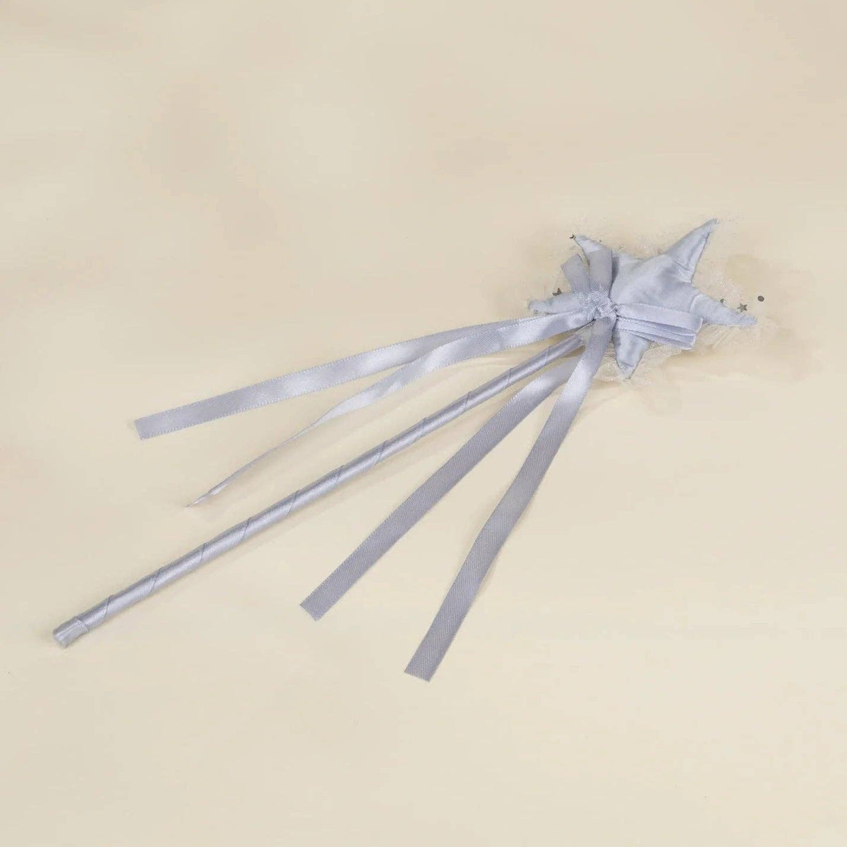 A light silver-gray fabric hair accessory with a small bow and long ribbon tails, laid flat on a warm beige background.
