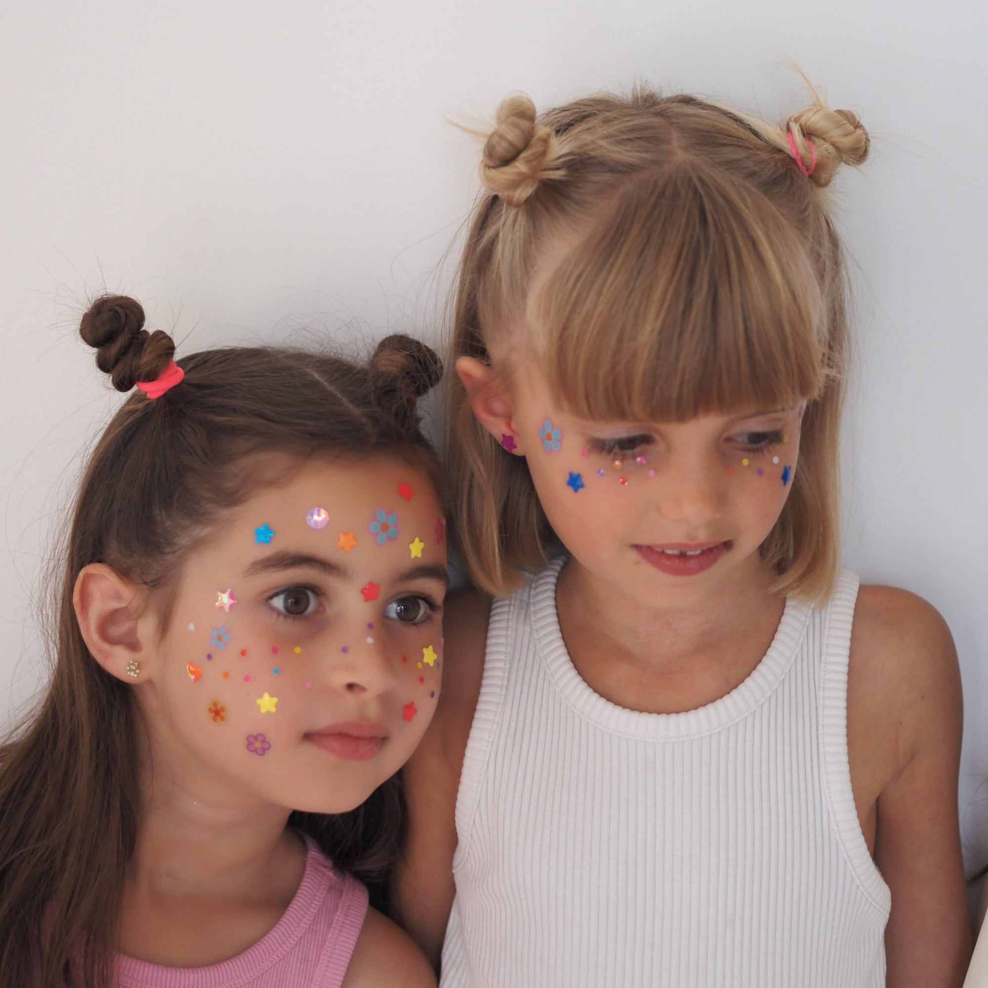 Two young girls with face paint sitting next to each other against a white background