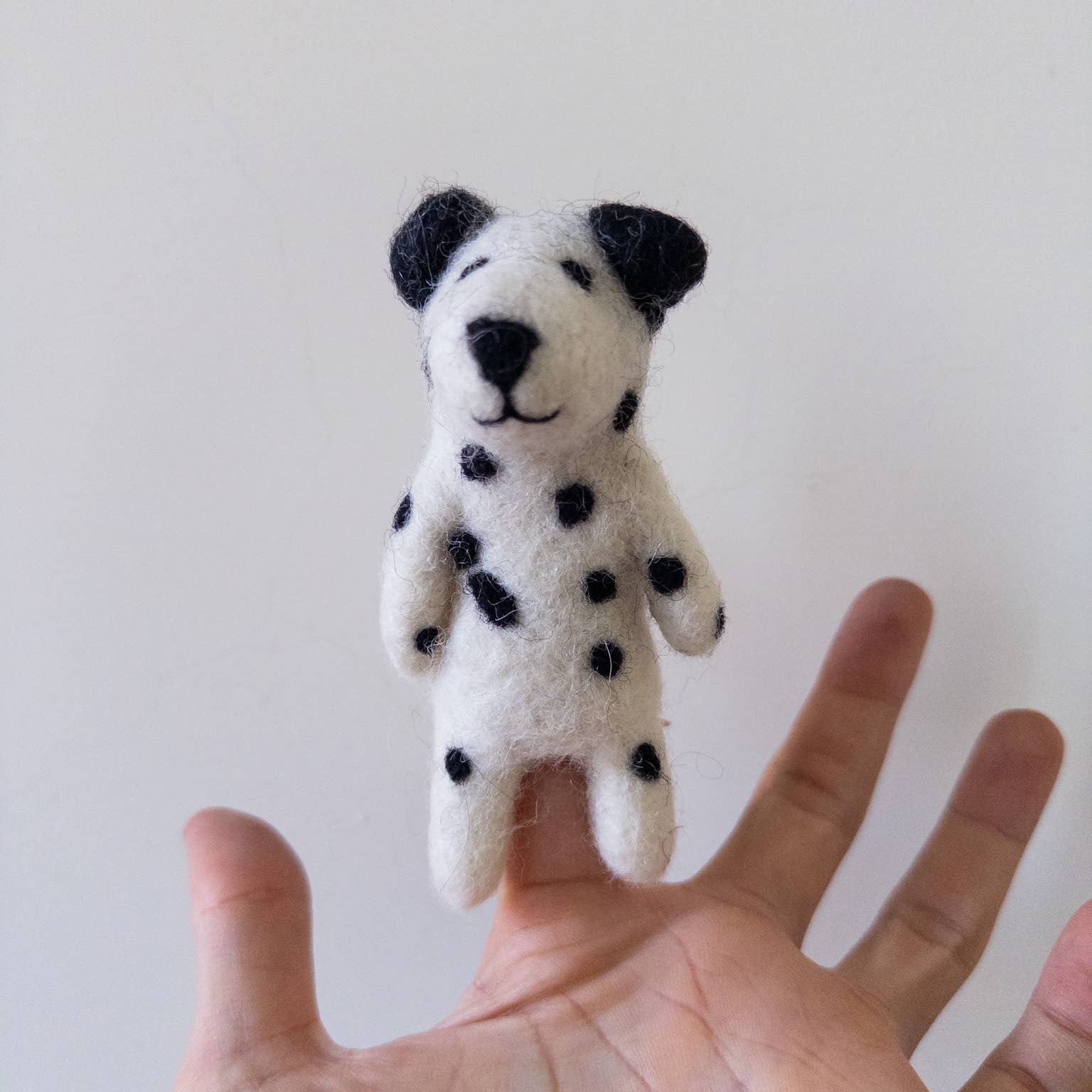 Small white dog toy with black spots held in a hand against a plain background