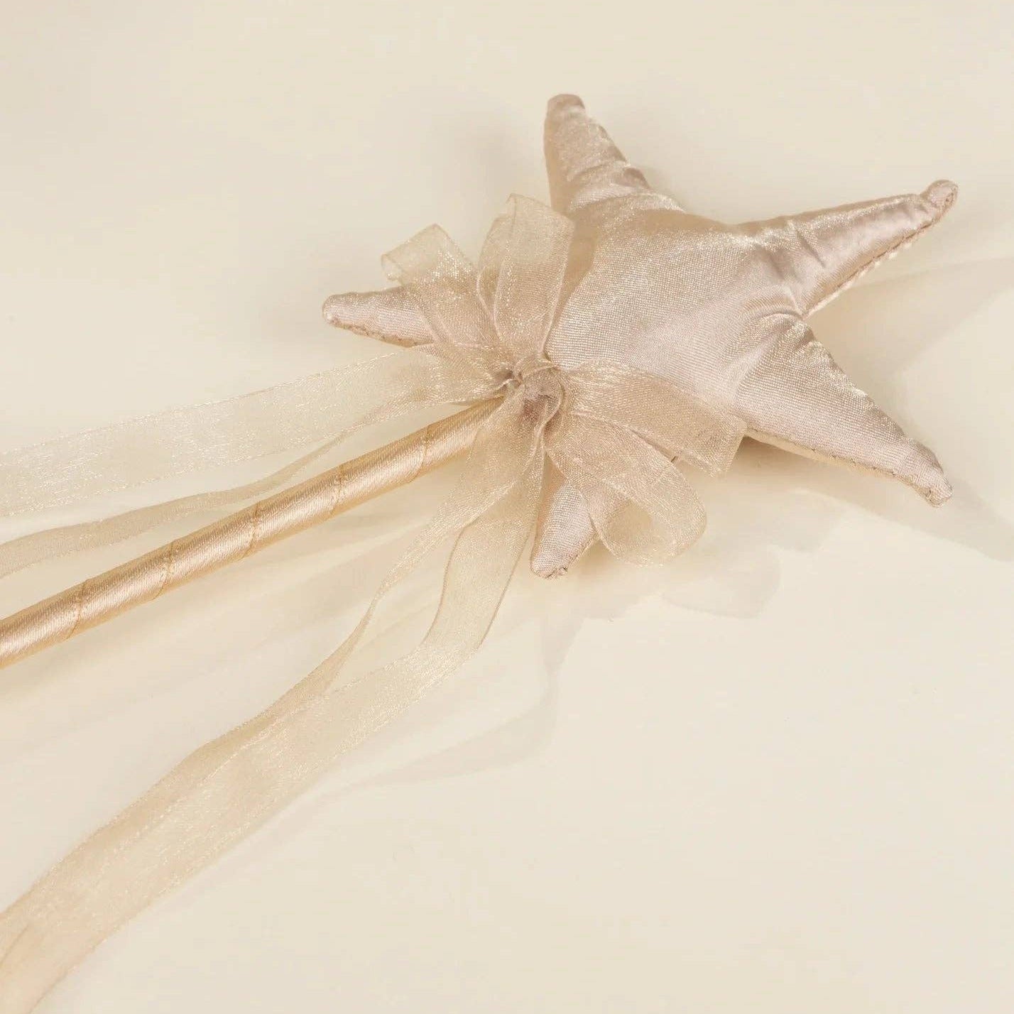 A star-shaped fabric wand topper in champagne satin with a matching sheer ribbon and bow, attached to a wooden stick, shown on a plain cream background.