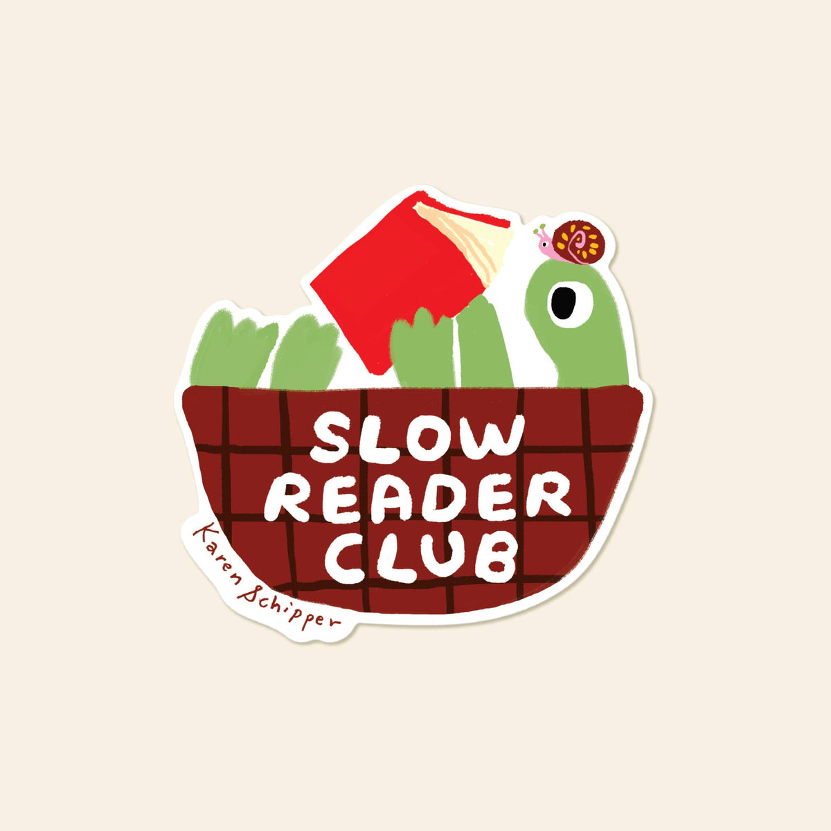 A die-cut sticker featuring a green cartoon frog holding a red book above a brown basket with the words 'SLOW READER CLUB' in white. A small signature reading 'Karen Schipper' appears on the lower left.