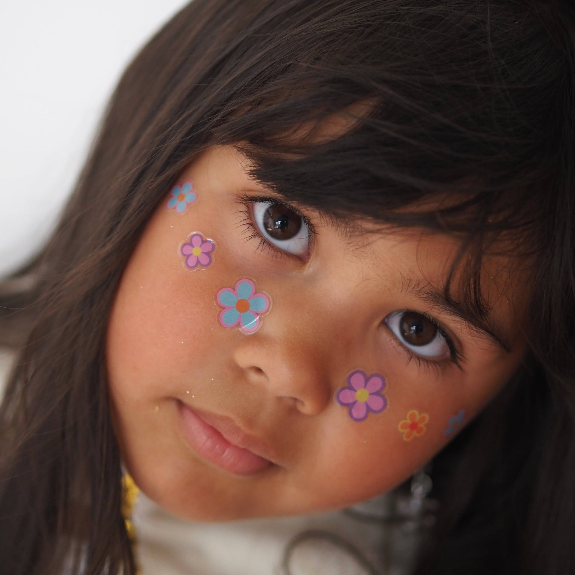 Young girl with colorful flower stickers on her face against a white background