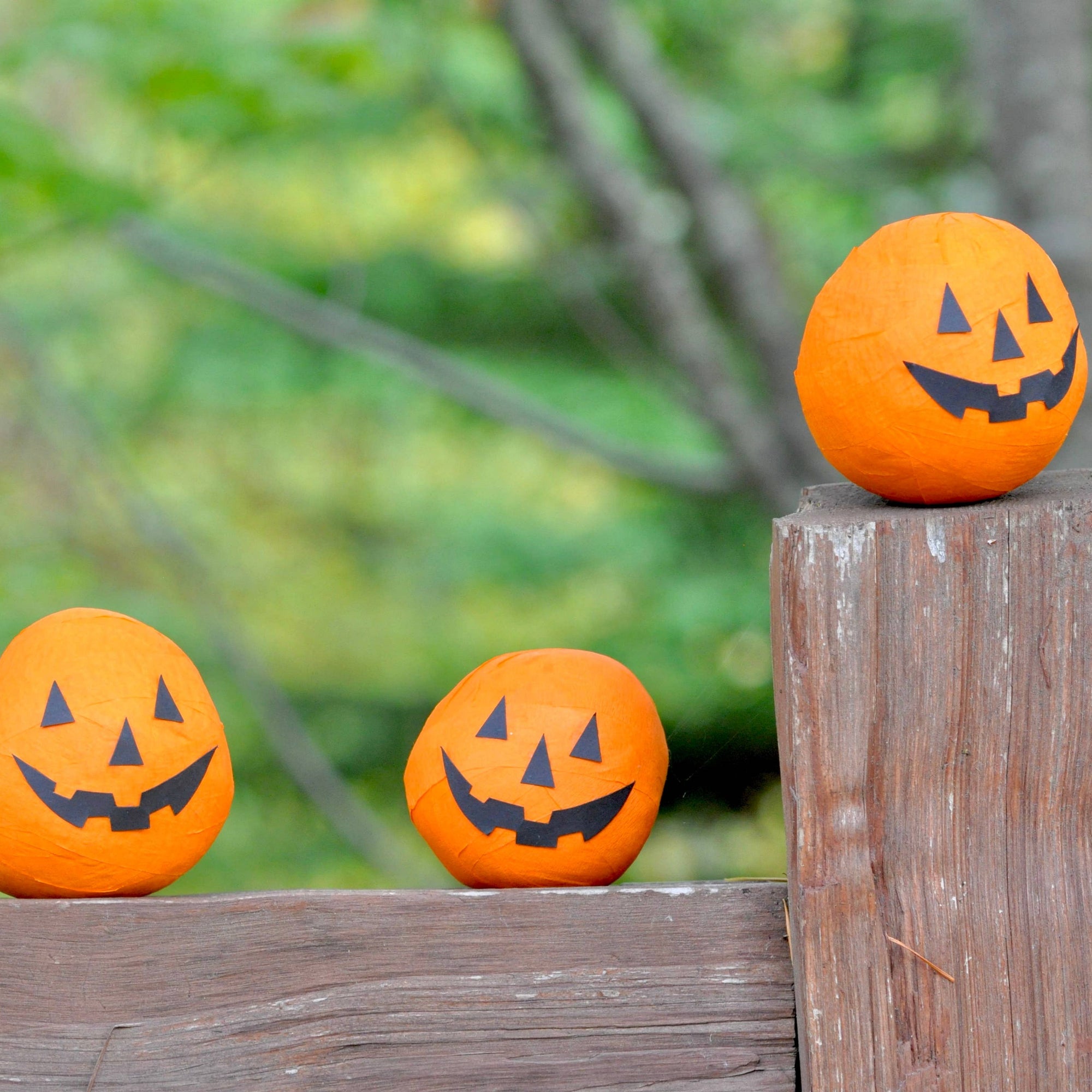 Three orange pumpkins with black faces on a wooden post against a blurred green background