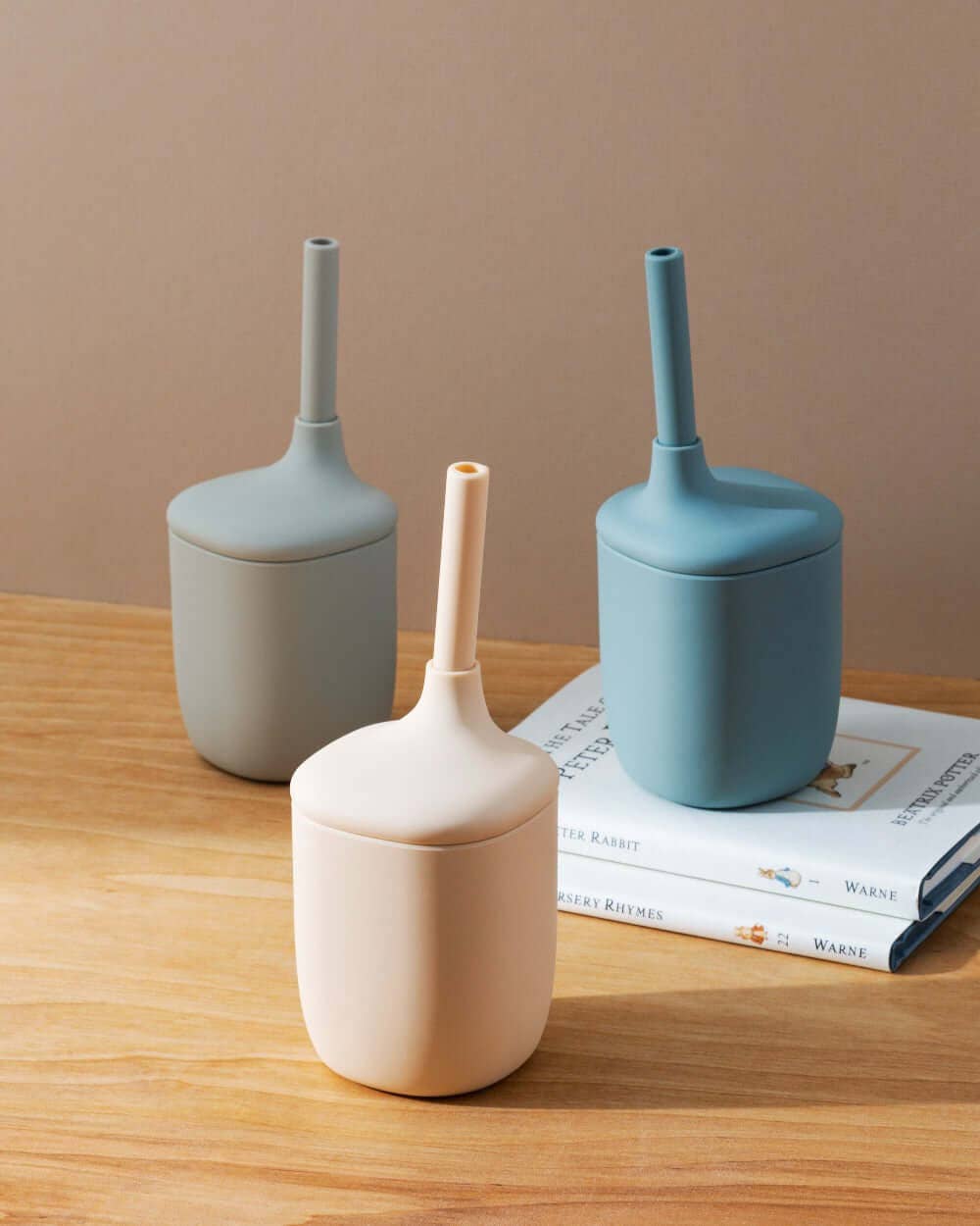 Three silicone cups in different colors on a wooden surface with books in the background.