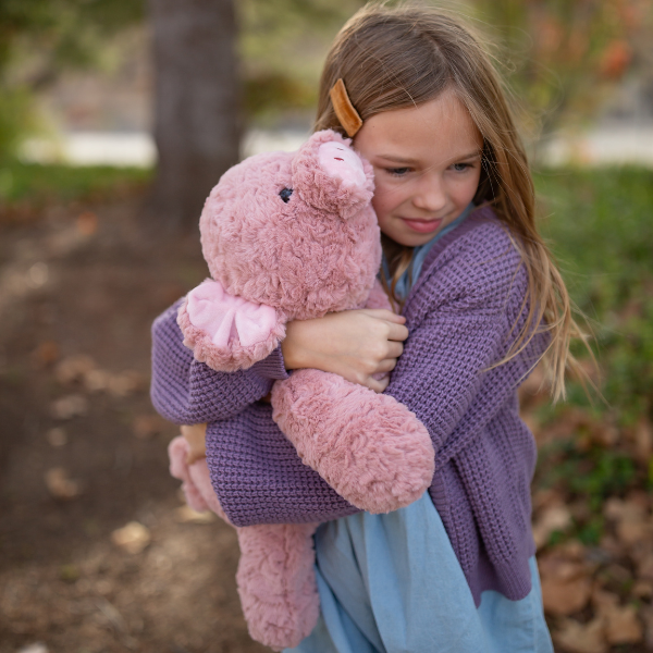 Young girl holding a pink teddy bear outdoors