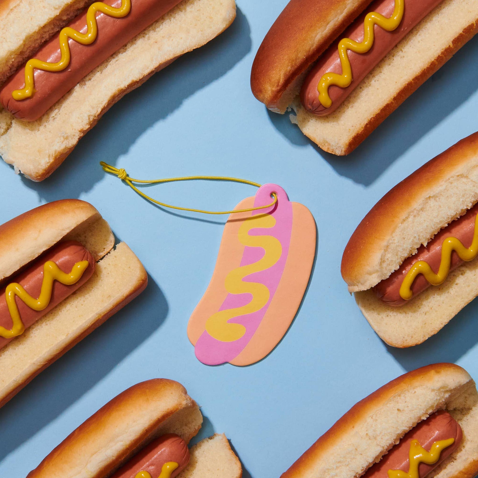 Hot dogs with mustard on buns arranged on a blue background with a hot dog-shaped keychain.