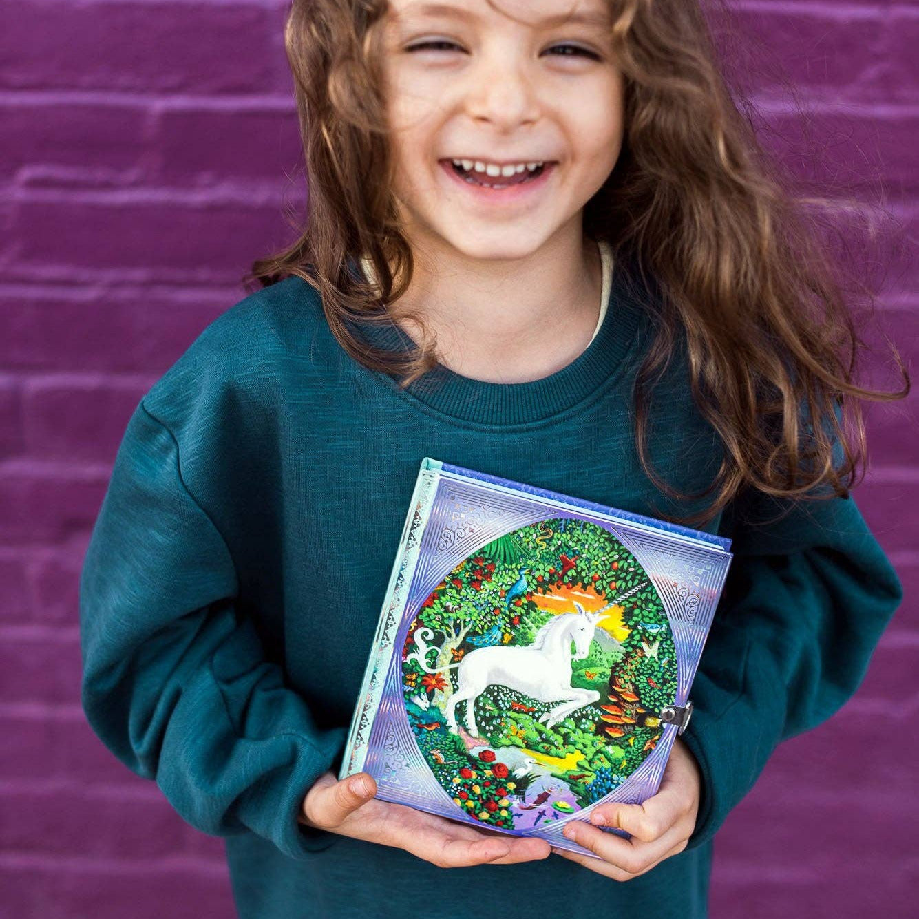 Child holding a book with a unicorn illustration against a purple brick wall