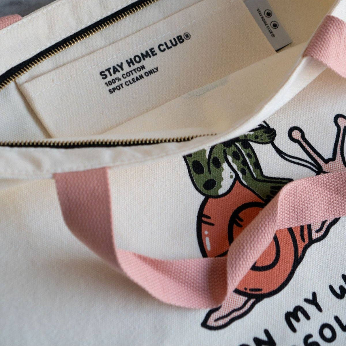 Close-up of a bag with 'Stay Home Club' branding and a cartoon design.