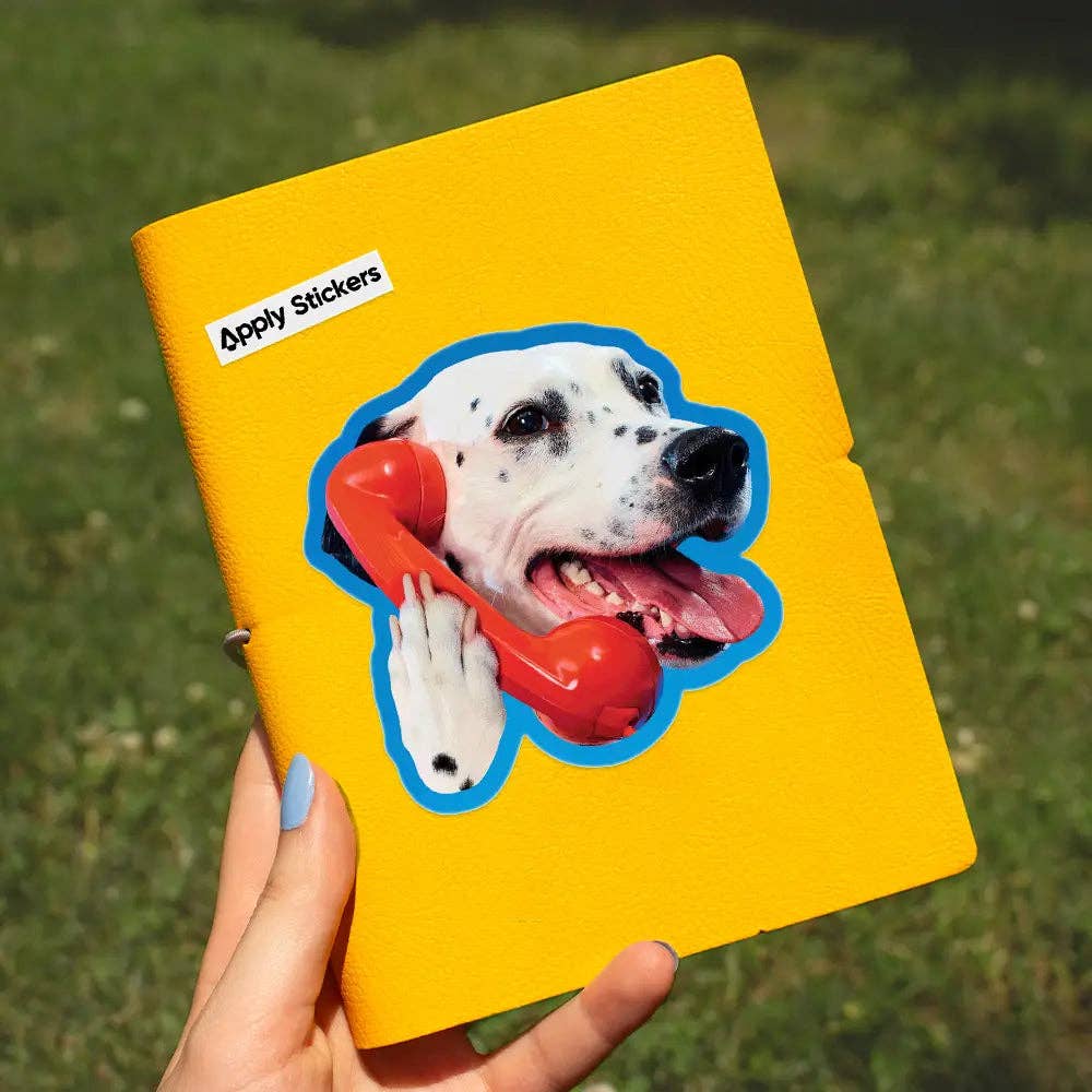 Yellow notebook with a dog sticker holding a red phone, held by a hand against a grassy background.