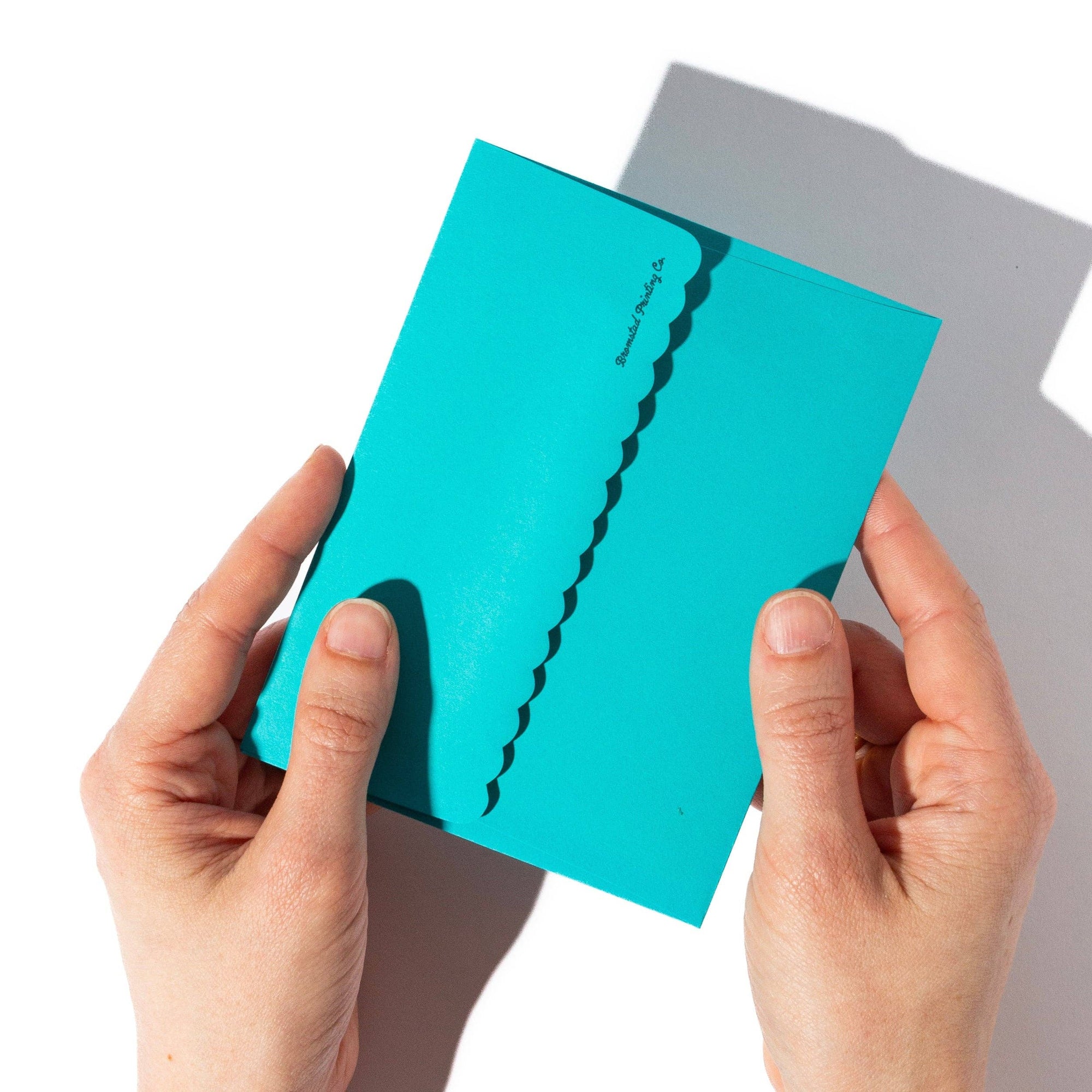 Hands holding a turquoise card with a wavy line design on a white background