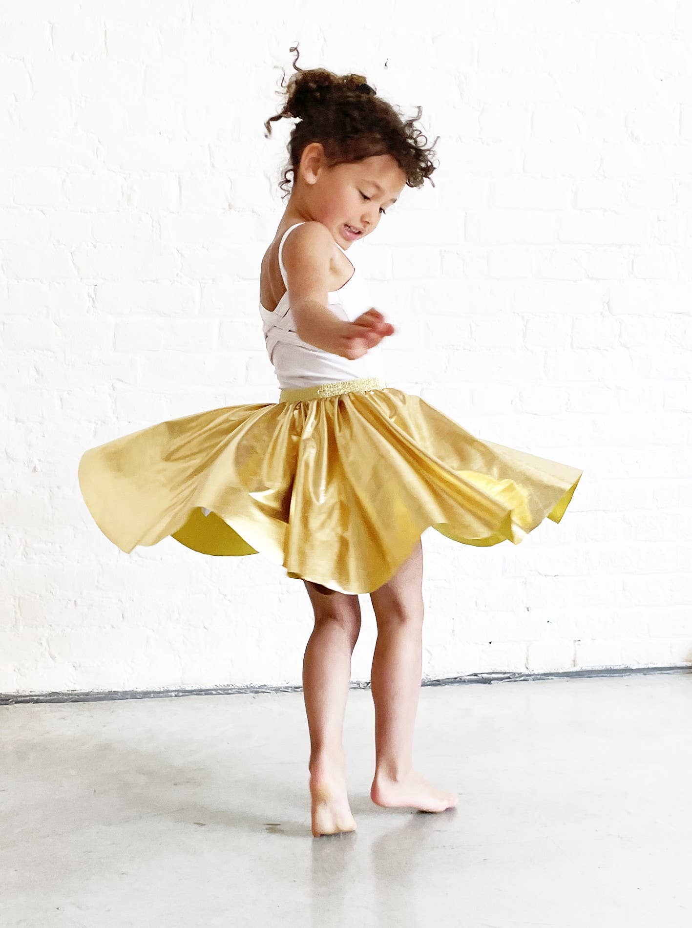 Child in a yellow skirt dancing on a white floor with a white wall background