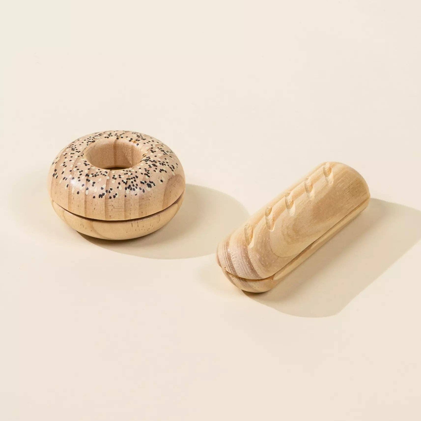 Wooden toy bagel with sprinkles and a wooden toy bread roll on a beige background