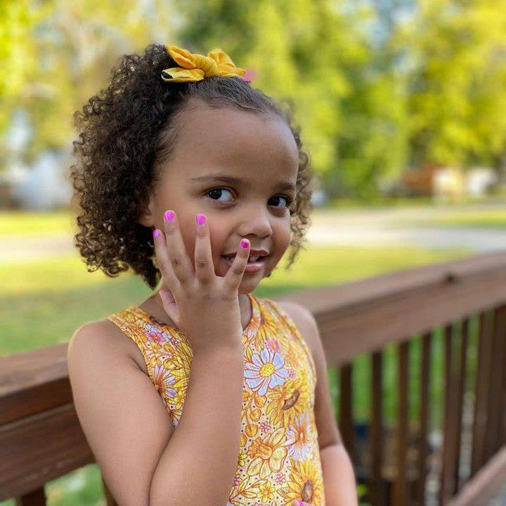 Young girl in a yellow floral dress standing outdoors on a wooden deck.