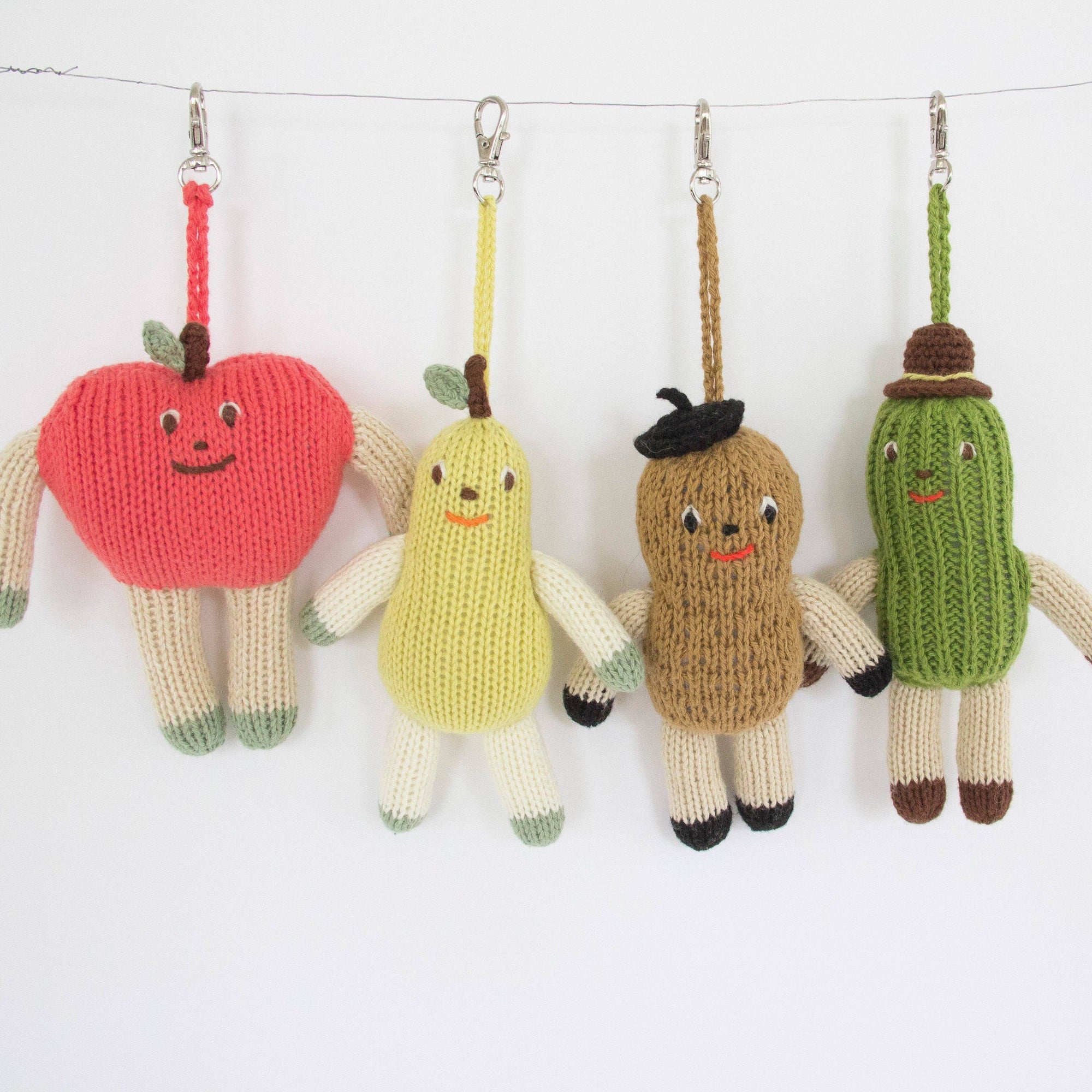 Knitted keychains shaped like an apple, banana, peanut, and pickle on a white background.