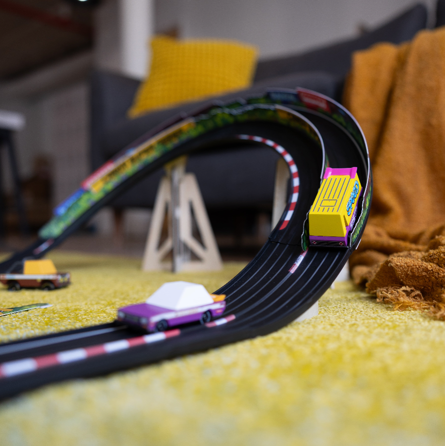 Toy car track set on a carpeted floor with toy cars on a blurred indoor background