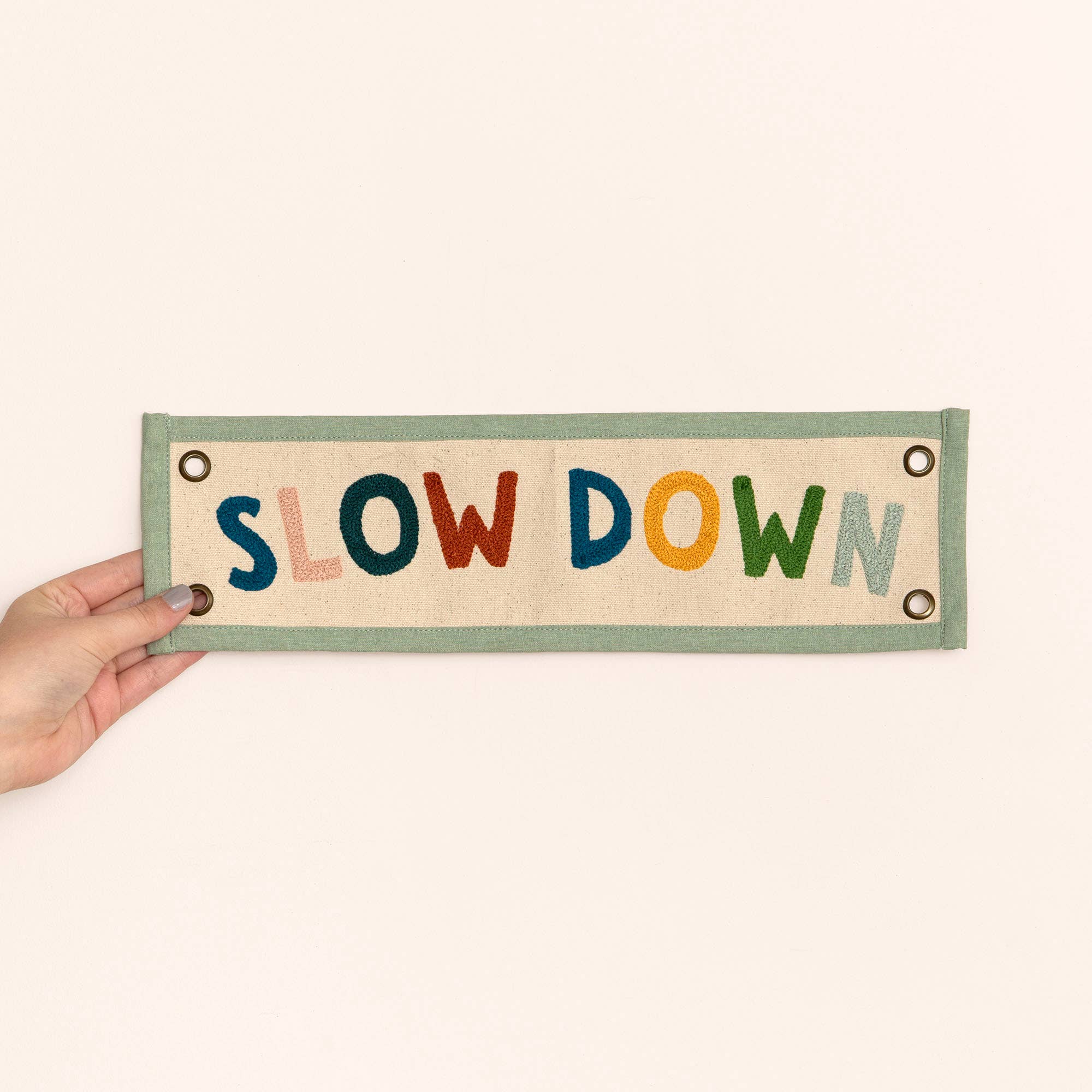 Hand holding a sign with 'SLOW DOWN' in colorful letters on a beige background