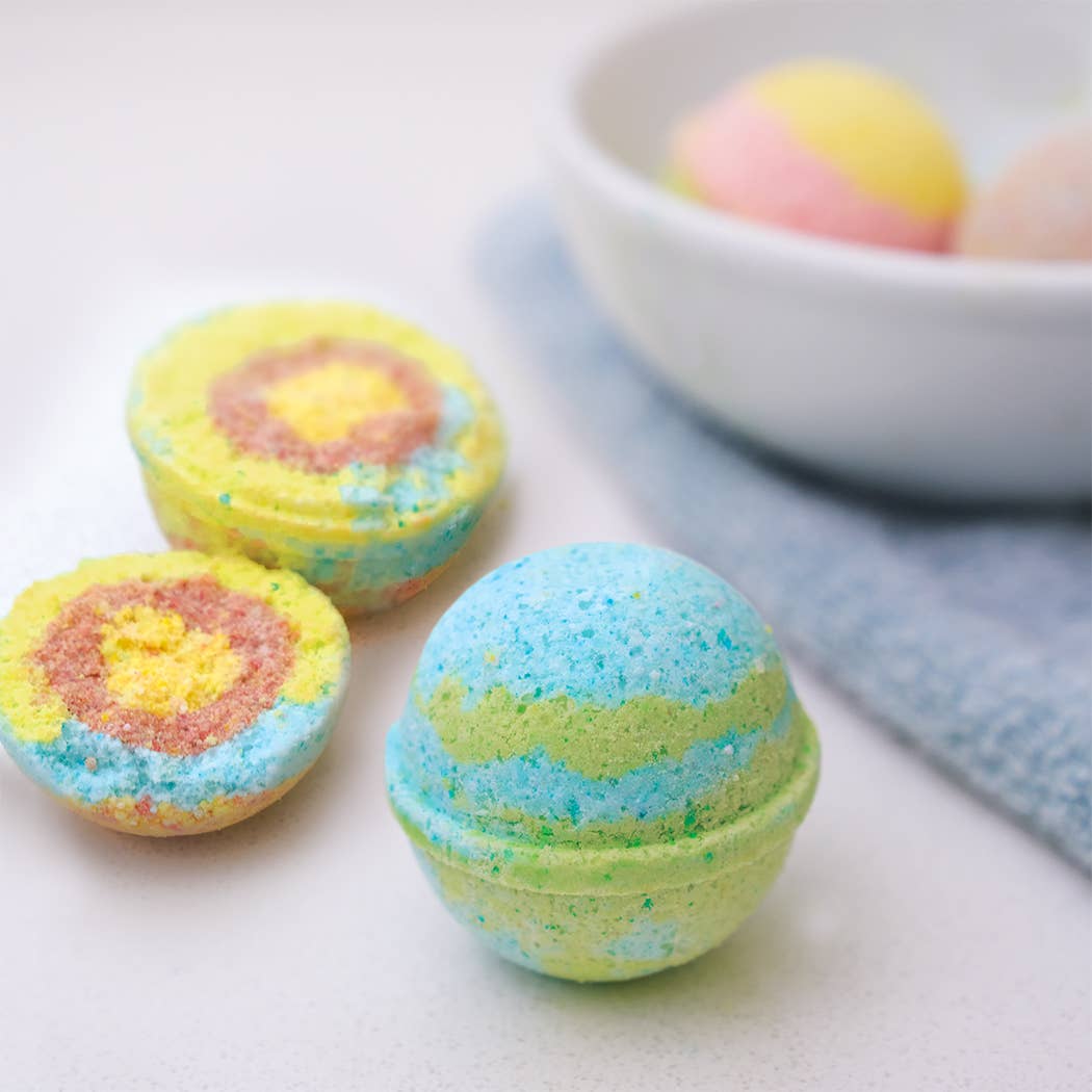 Colorful bath bombs on a white surface with a bowl in the background