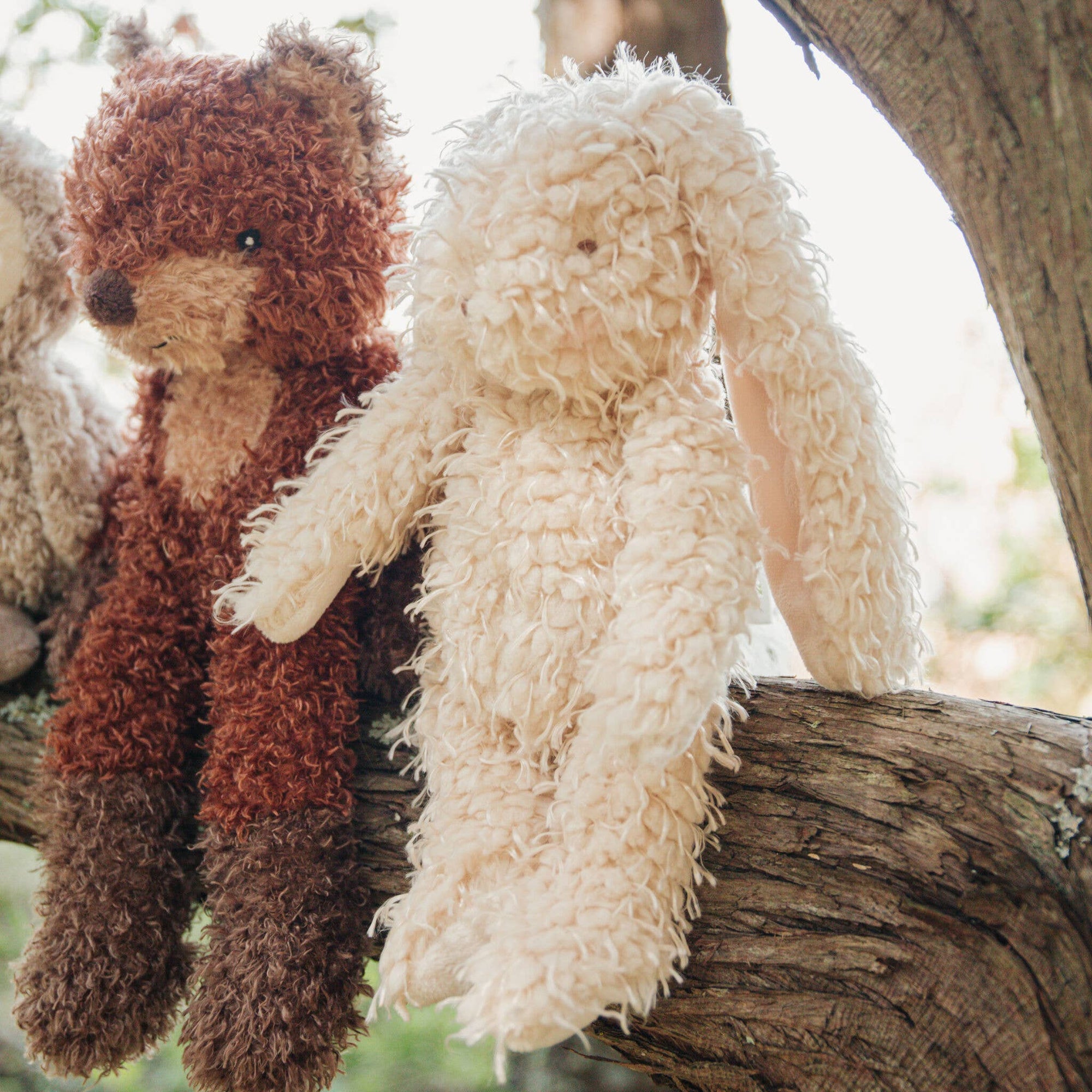 Two plush toys, one brown and one white, sitting on a wooden branch with a natural background.