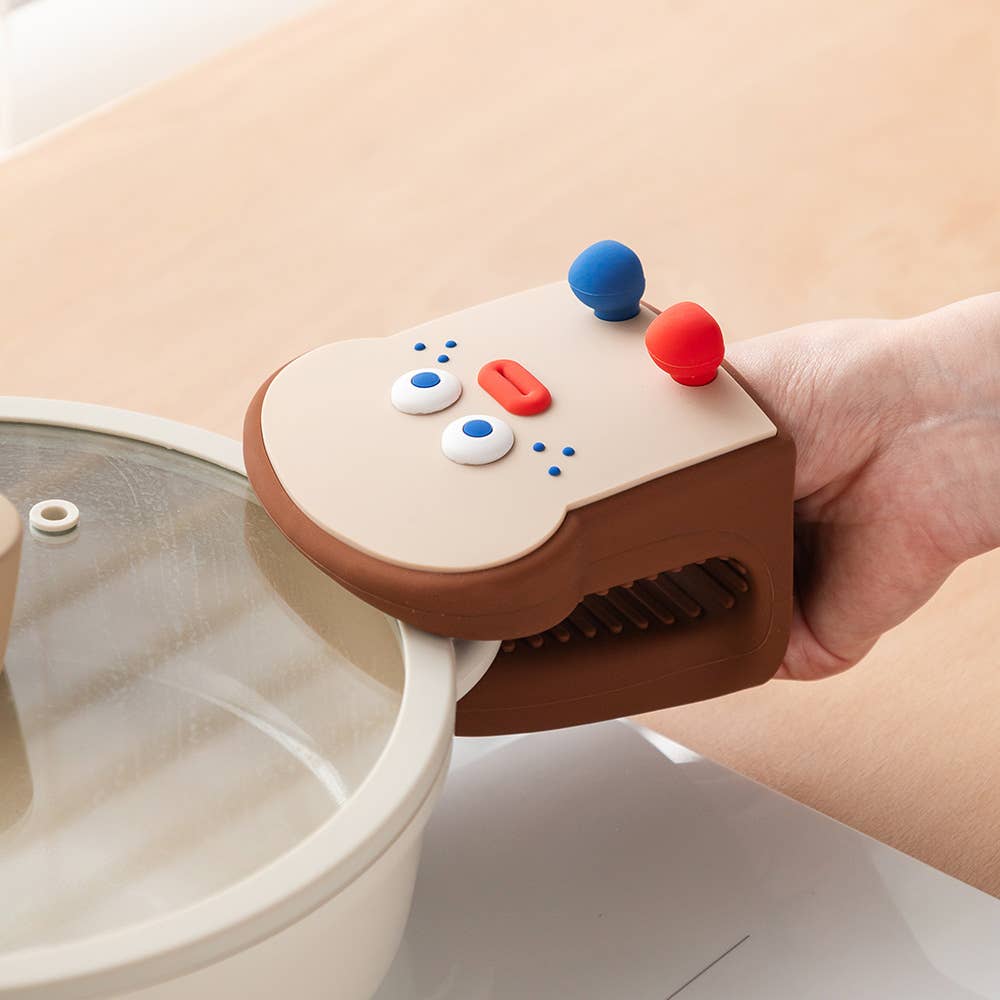 Hand holding a small, colorful oven mitt over a white pot with a beige background