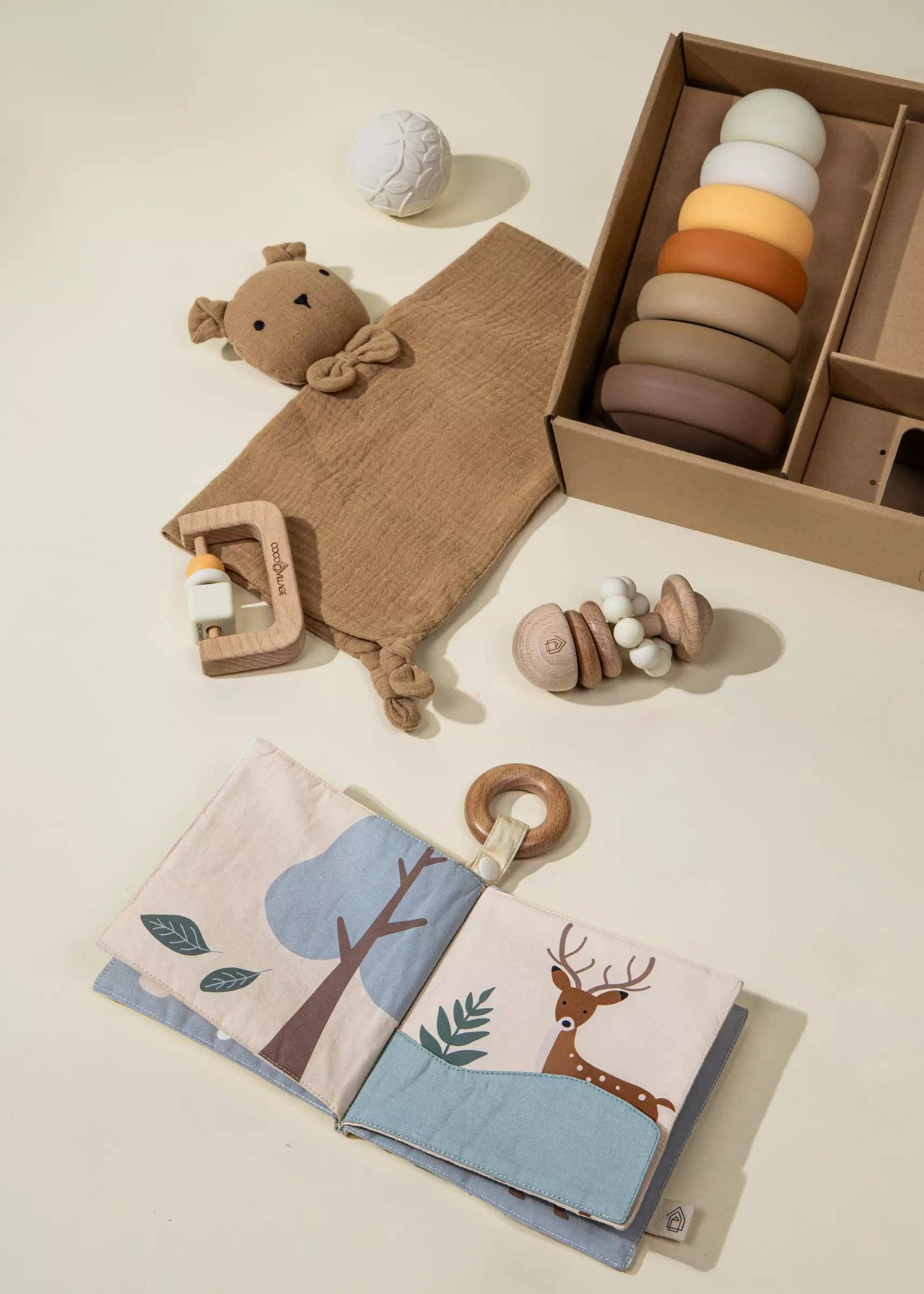 Collection of wooden toys including a teething ring, ring stacker, and fabric book on a light surface.