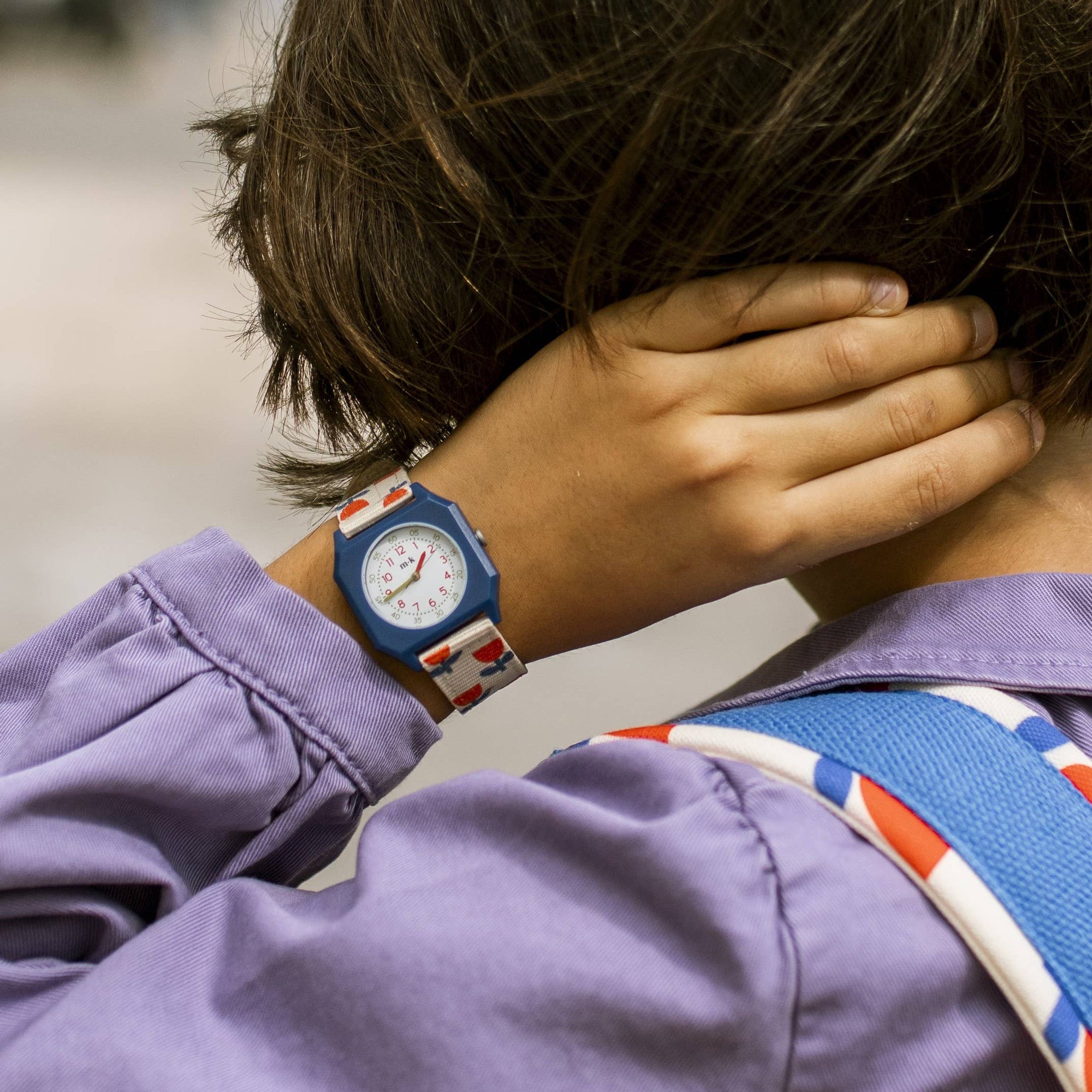 Person wearing a purple jacket with a colorful strap over their shoulder, covering part of their face.