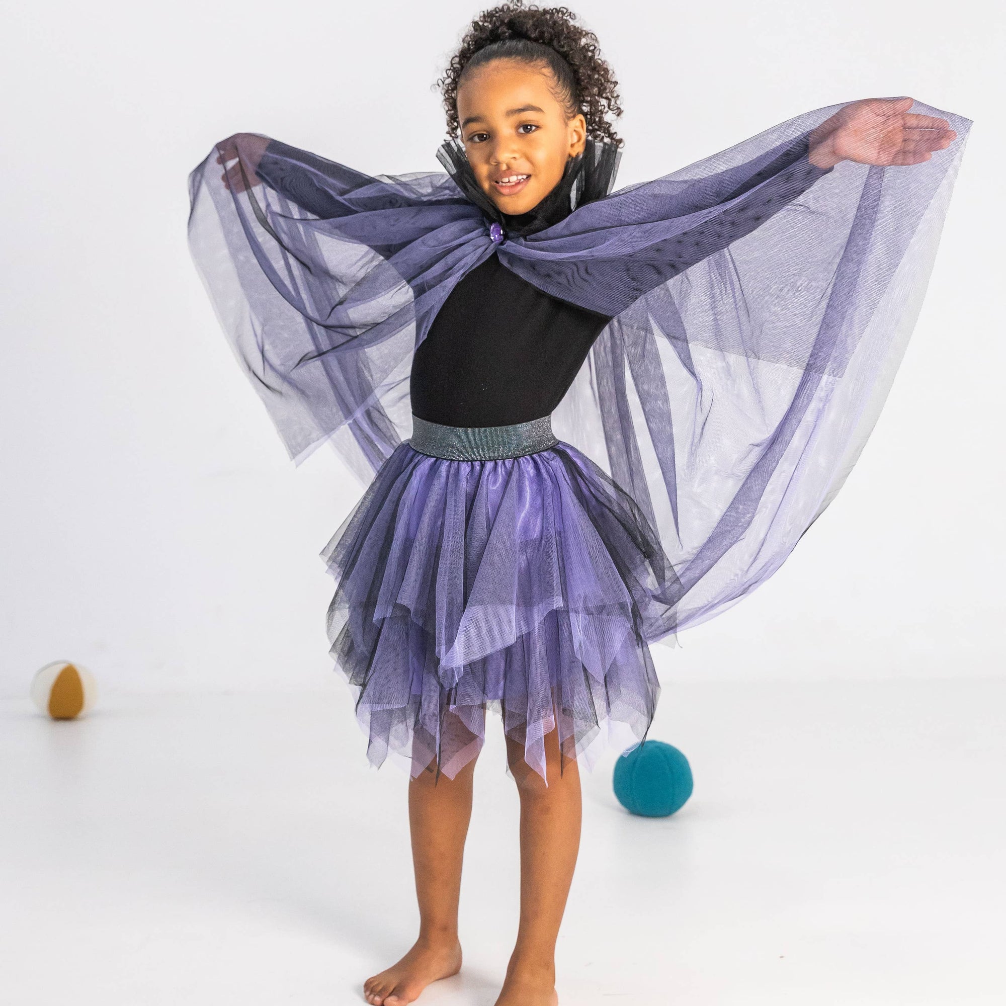 Child wearing a black outfit with a sheer purple overlay on a white background